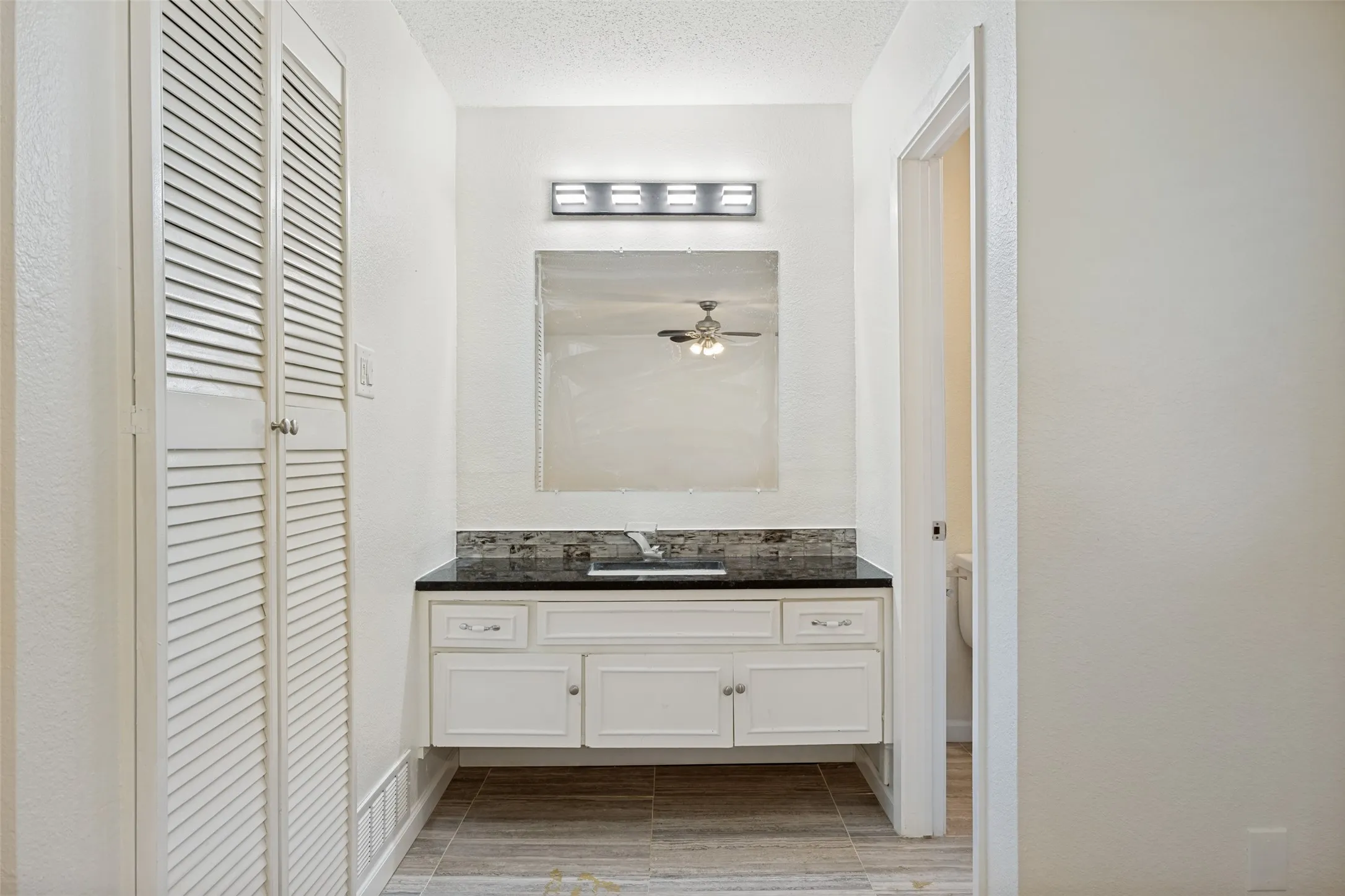 White vanity with dark countertop and mosaic tile backsplash, featuring a rectangular mirror with overhead light fixture