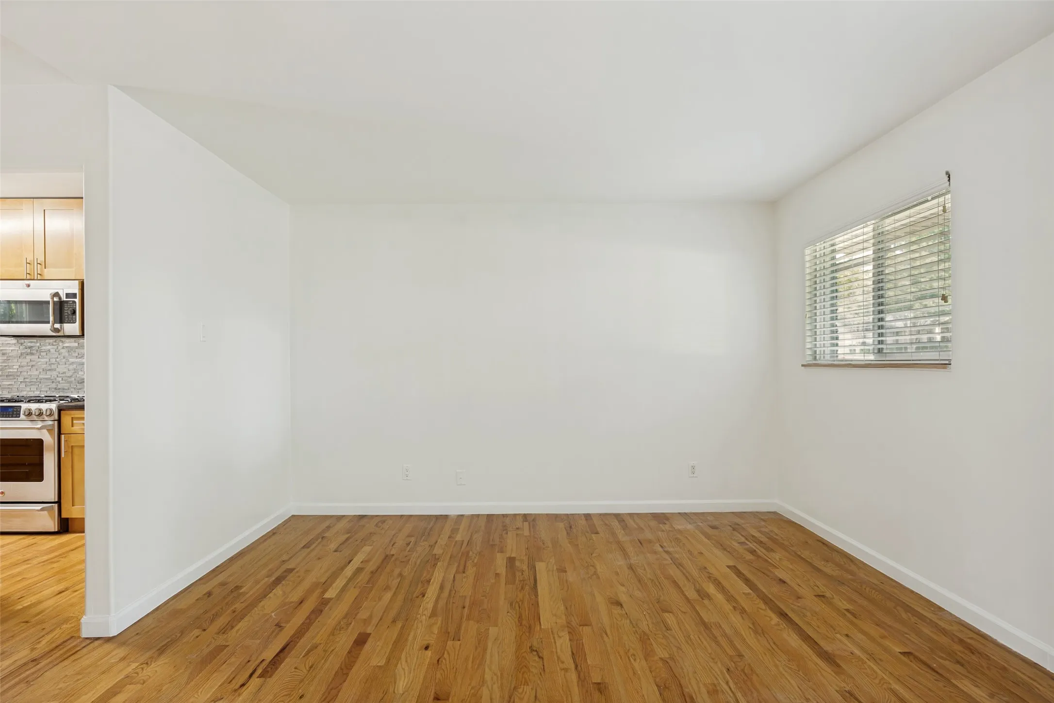 Spacious room featuring wood-finish flooring and a large window with horizontal blinds
