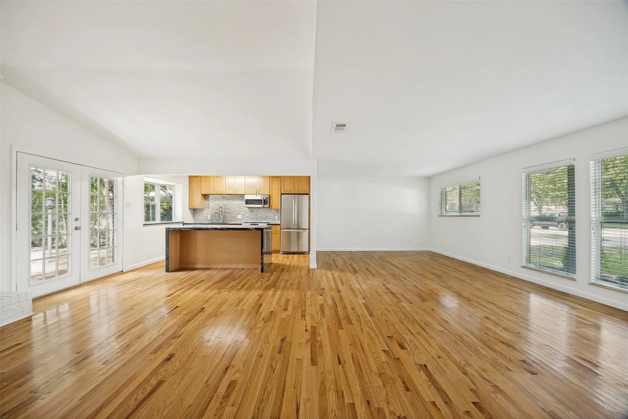 Open concept living area featuring wood-finish flooring throughout, a vaulted white ceiling, and white walls