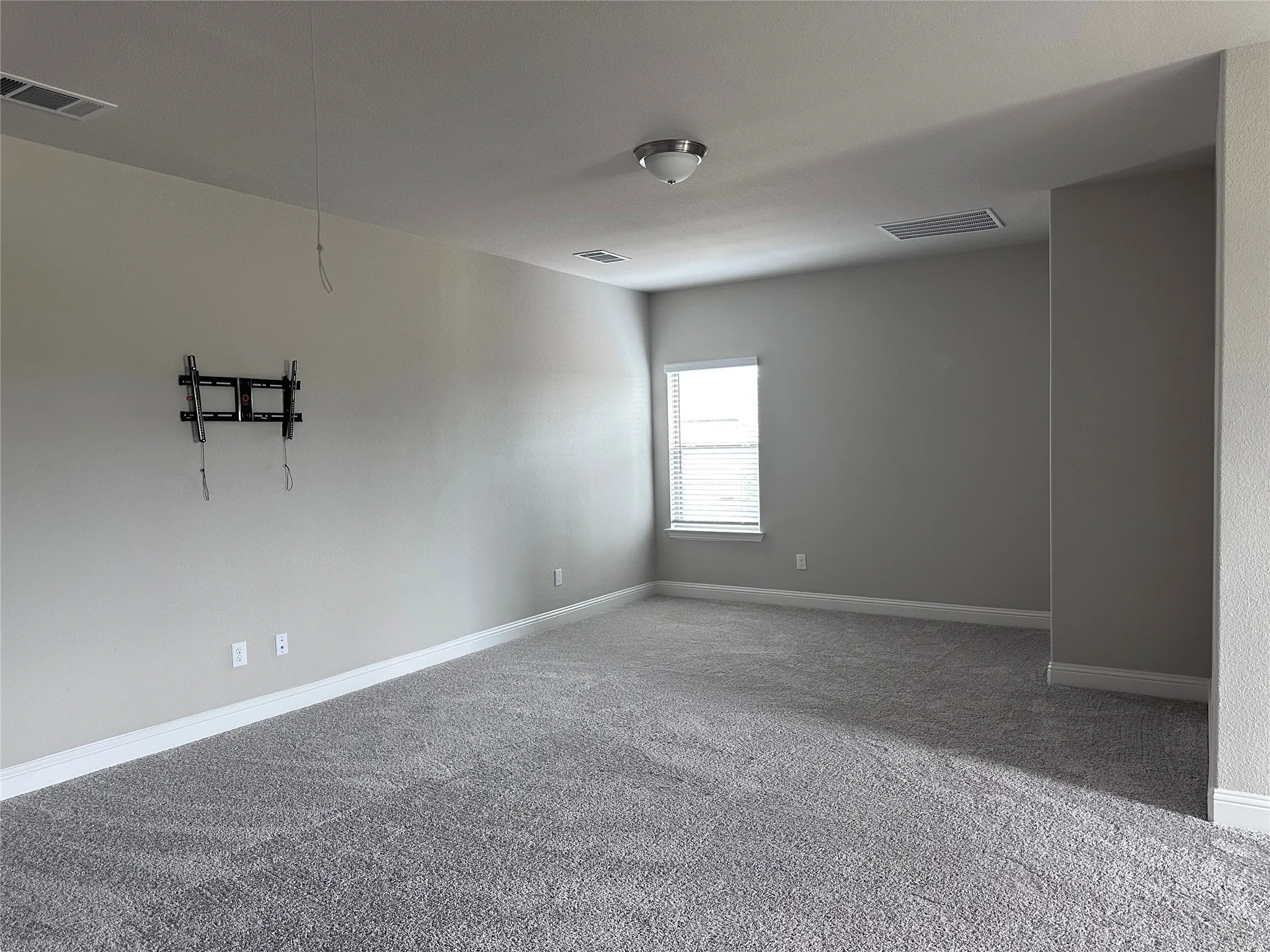 Spacious room featuring neutral wall paint, gray carpeting, a single window with blinds, and a flush mount ceiling light
