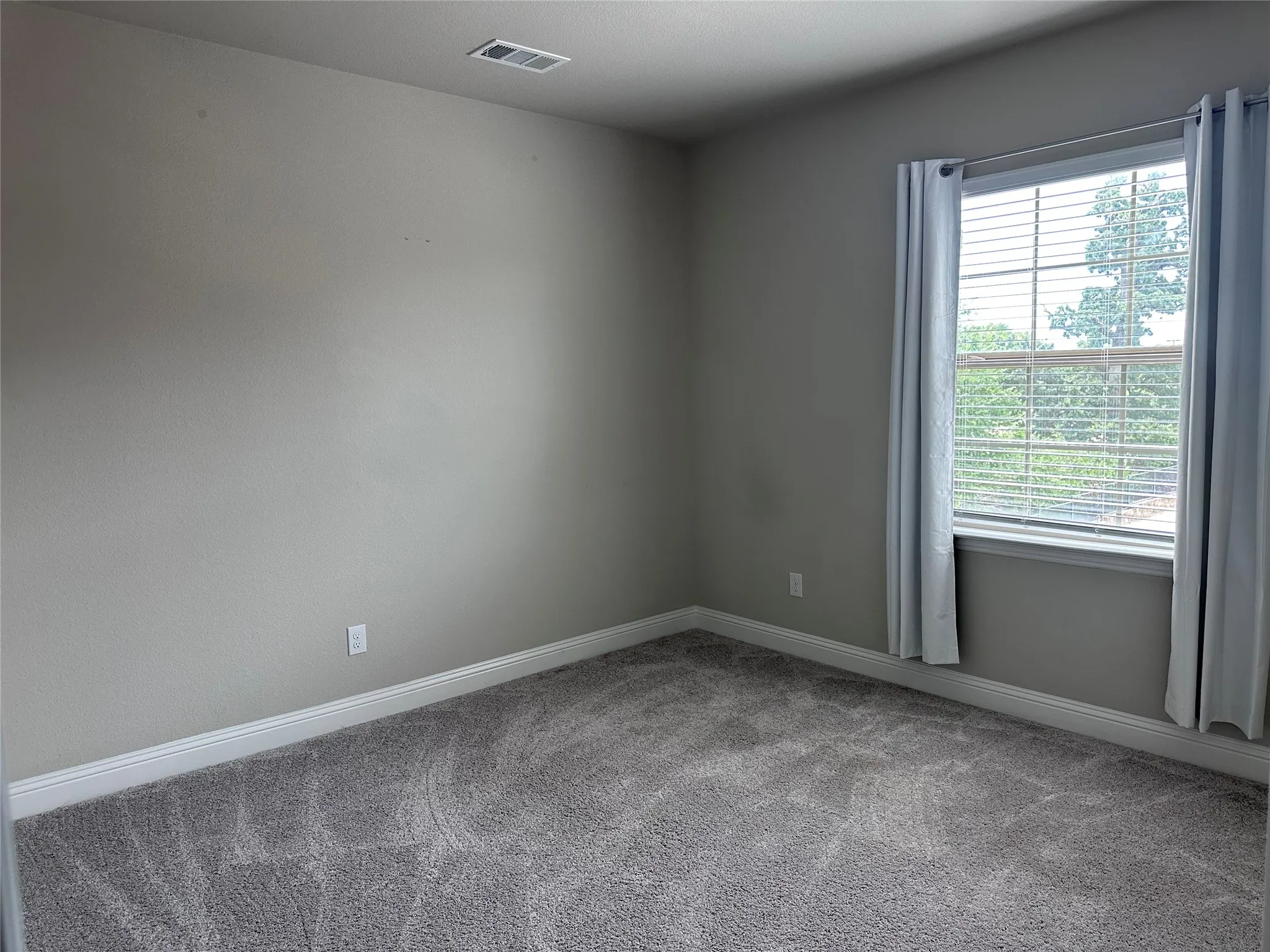 Spacious room featuring neutral carpeting, light gray walls, a window with blinds, and white trim