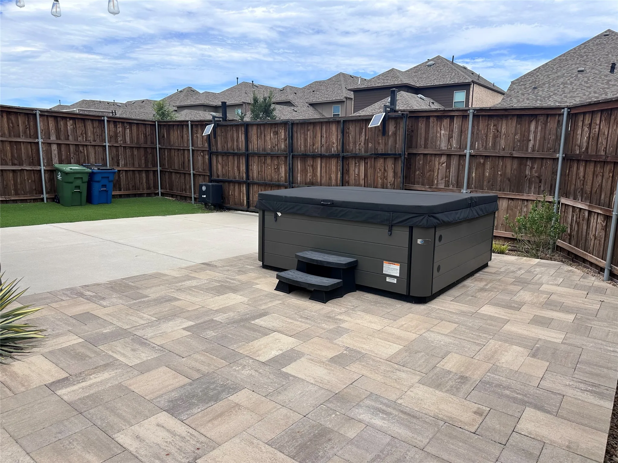 Expansive paver patio featuring a built-in spa, complemented by a concrete patio and a manicured lawn area