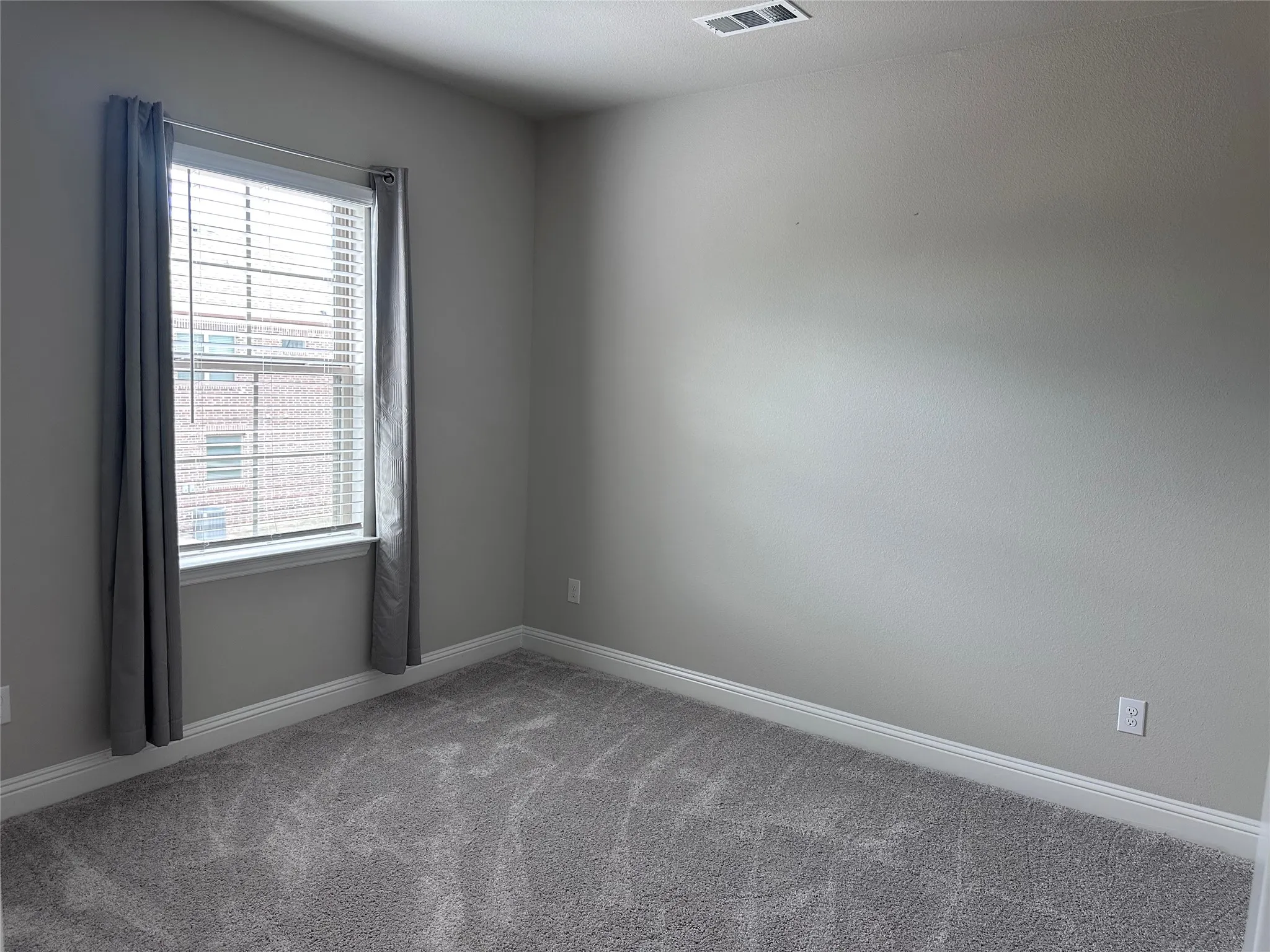 Carpeted room featuring a single window with blinds, light gray walls, white baseboards, and a ceiling vent
