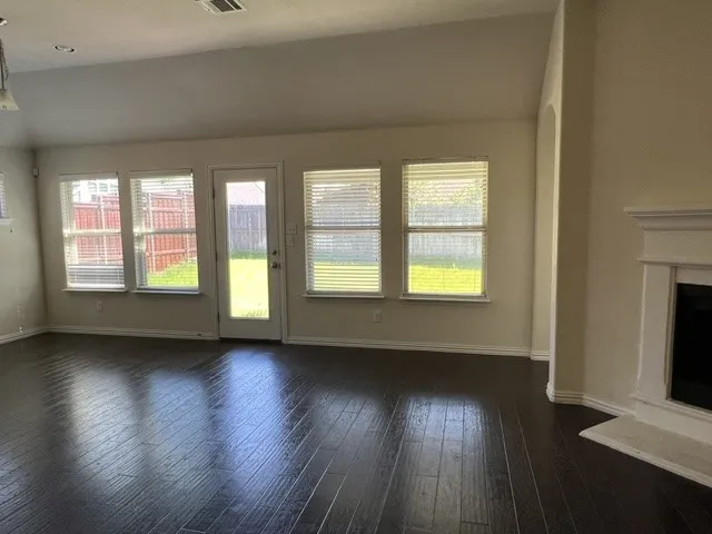 Spacious room featuring dark wood-finish flooring, multiple windows with blinds, a white door leading to the backyard, a white fireplace with a mantel, and recessed lighting