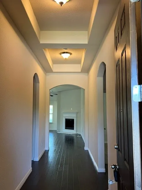 Entryway featuring a dark wood-finish floor, tray ceiling with semi-flush mount lighting, and arched doorways