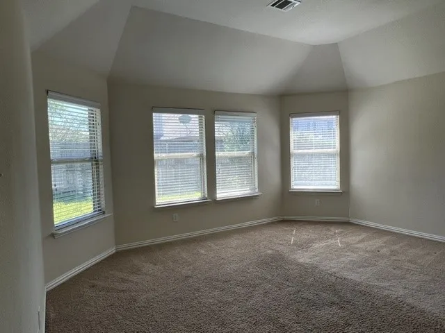Spacious room with a vaulted ceiling, multiple windows with blinds, light-colored walls, and brown carpeting