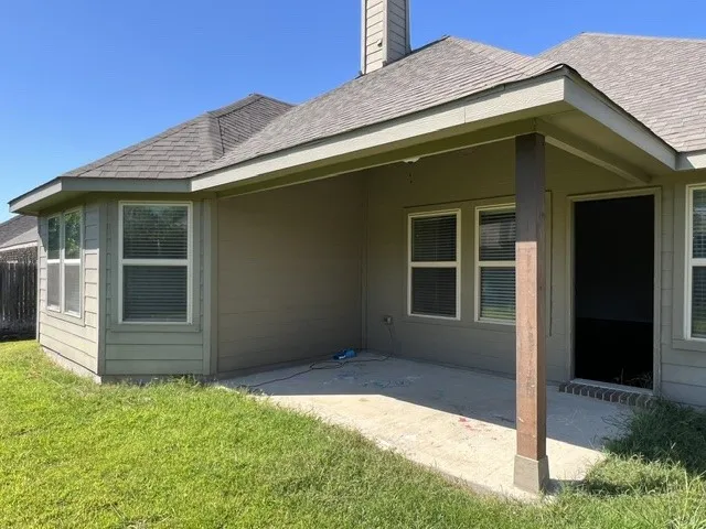 Rear exterior featuring a covered patio with a supporting pillar, concrete slab, and access to the interior