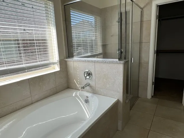Built-in tub with chrome fixtures and tiled surround, complemented by a glass-enclosed shower with a matching tiled base