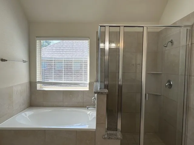 Bathroom featuring a built-in soaking tub with tile surround, a separate glass-enclosed shower with tiled walls and built-in shelving, and a window with blinds