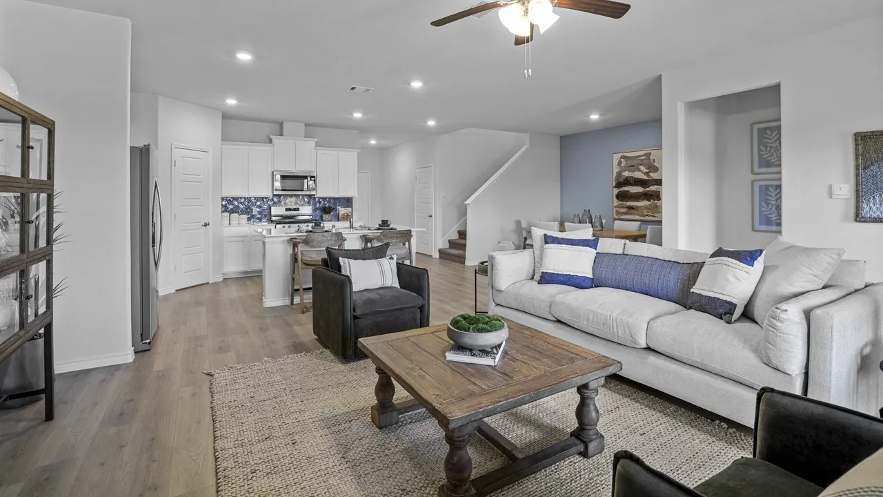 Open-concept living space featuring wood-finish flooring, recessed lighting, a ceiling fan, a white kitchen with a blue tile backsplash, and a dining area