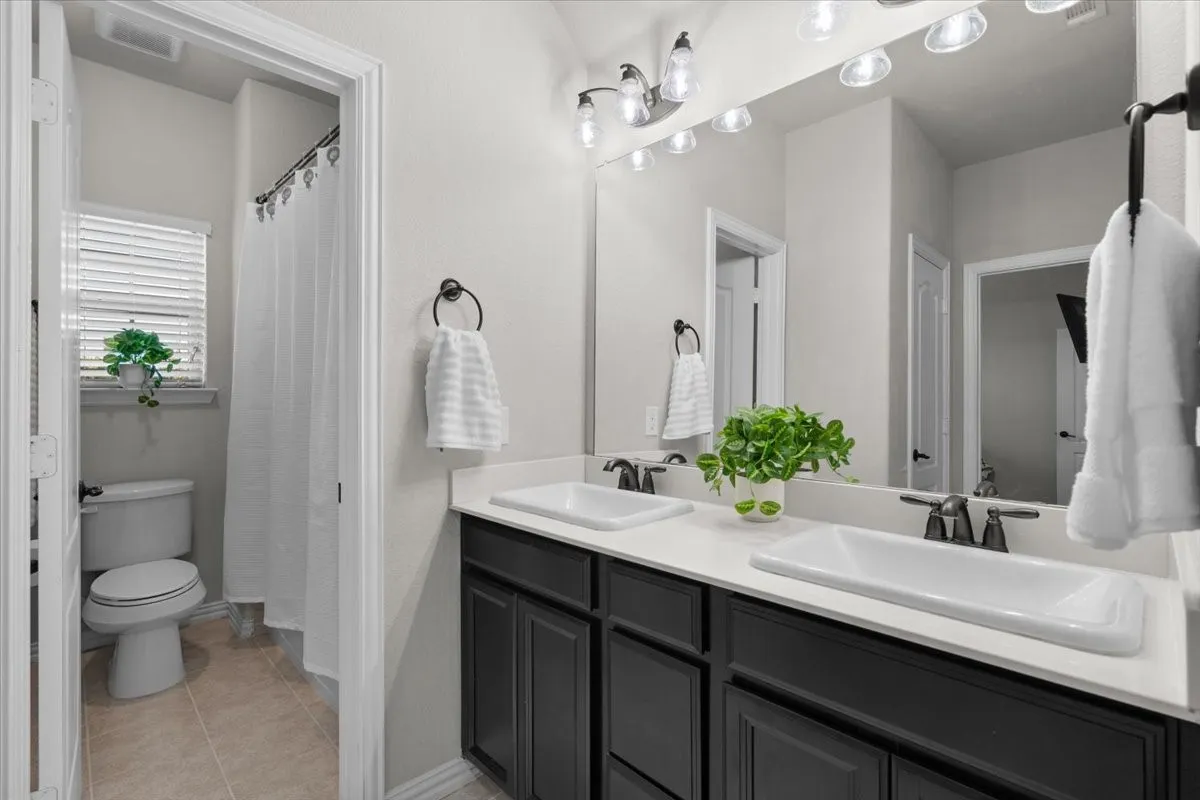 Bright bathroom with dual sinks and a private tub/shower room