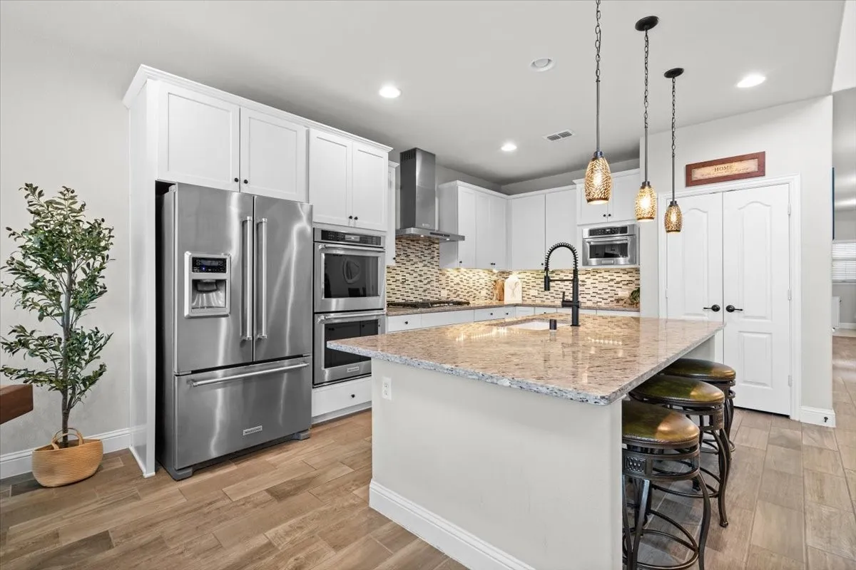 Gourmet kitchen with stainless steel appliances including double ovens, refrigerator, and 5 burner cook top