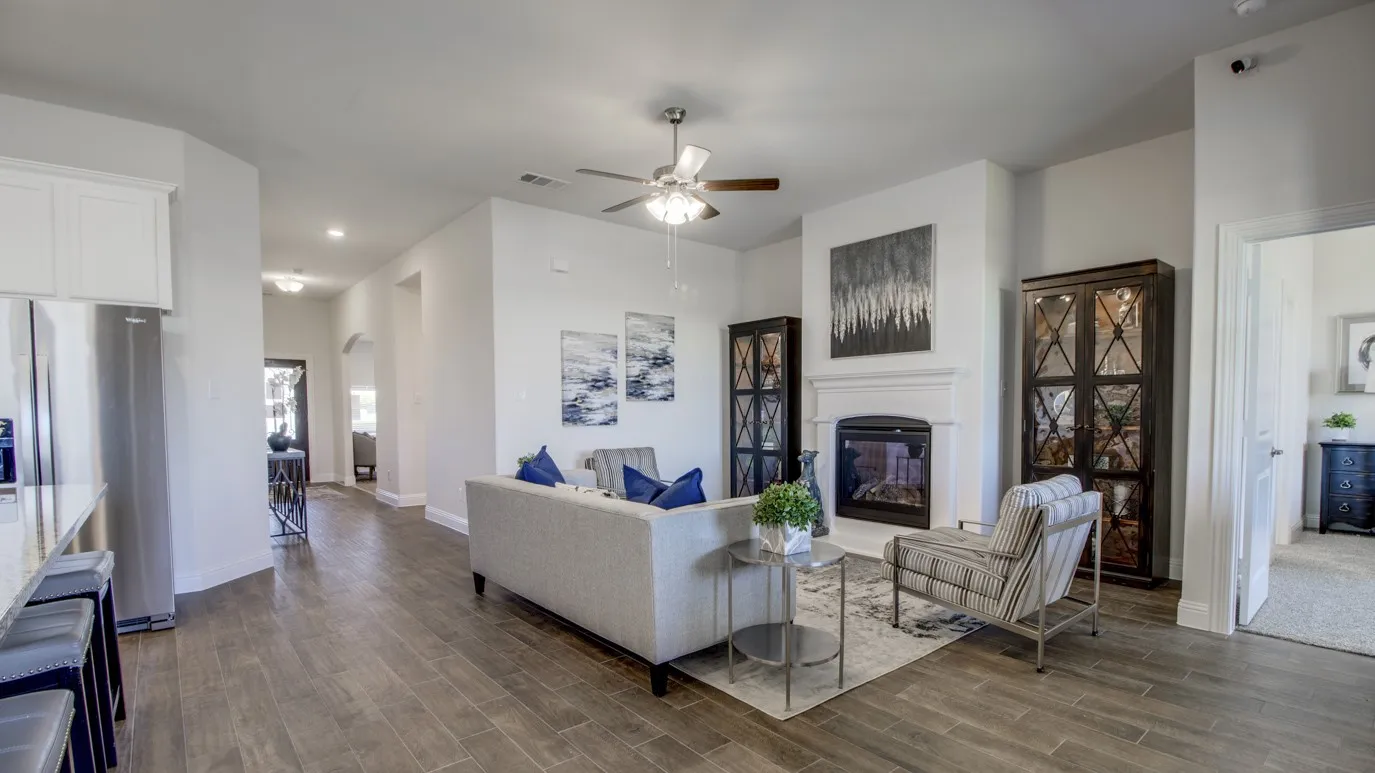 Living area featuring wood-finish flooring, a white mantel fireplace, and a ceiling fan