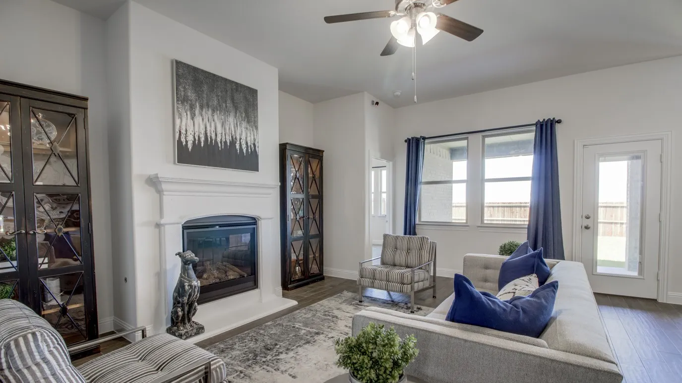 Living space featuring a white mantel fireplace, wood-finish flooring, ceiling fan, and multiple windows