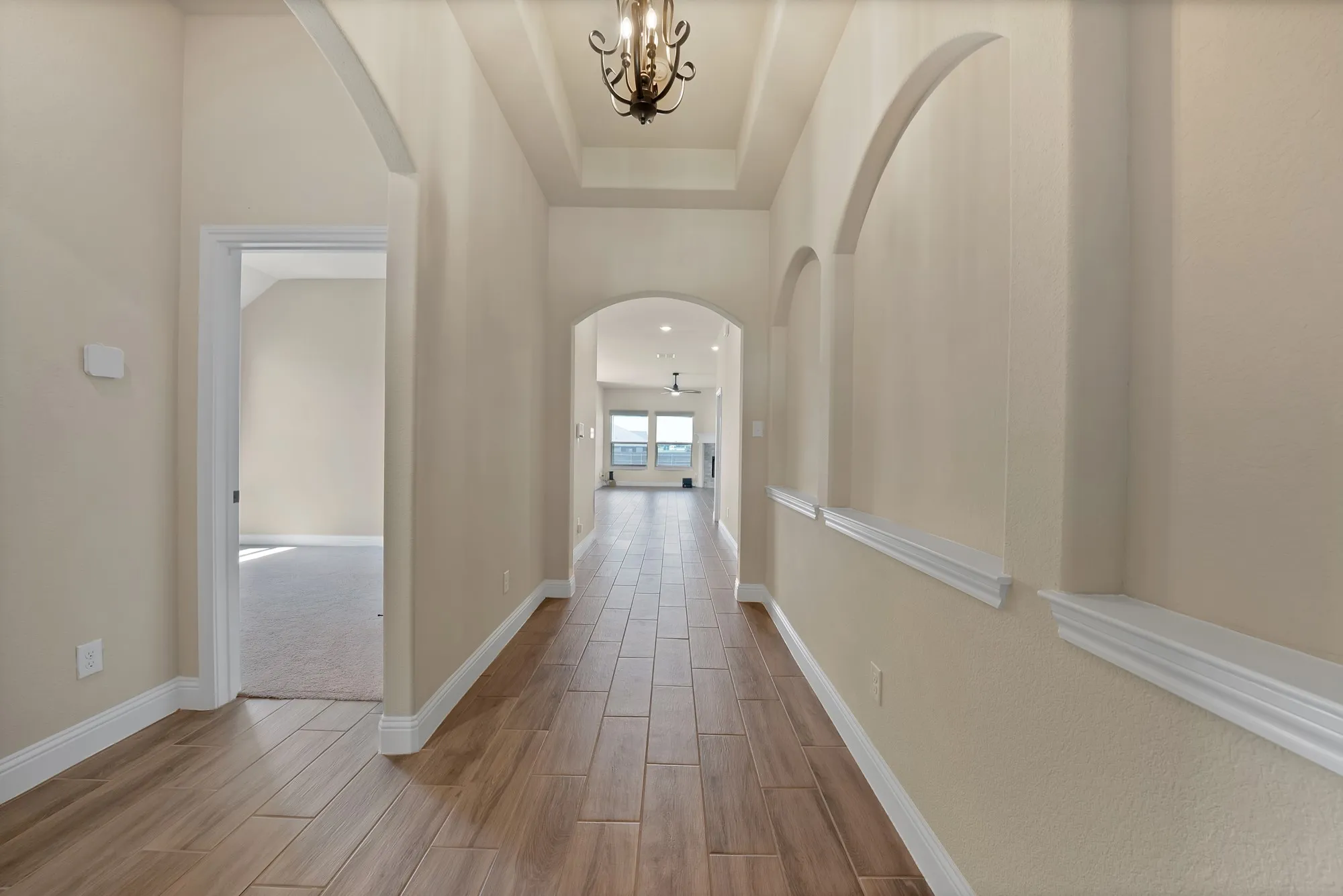 Hallway featuring wood-finish tile flooring, arched wall details, crown molding, and a tray ceiling with an ornate chandelier