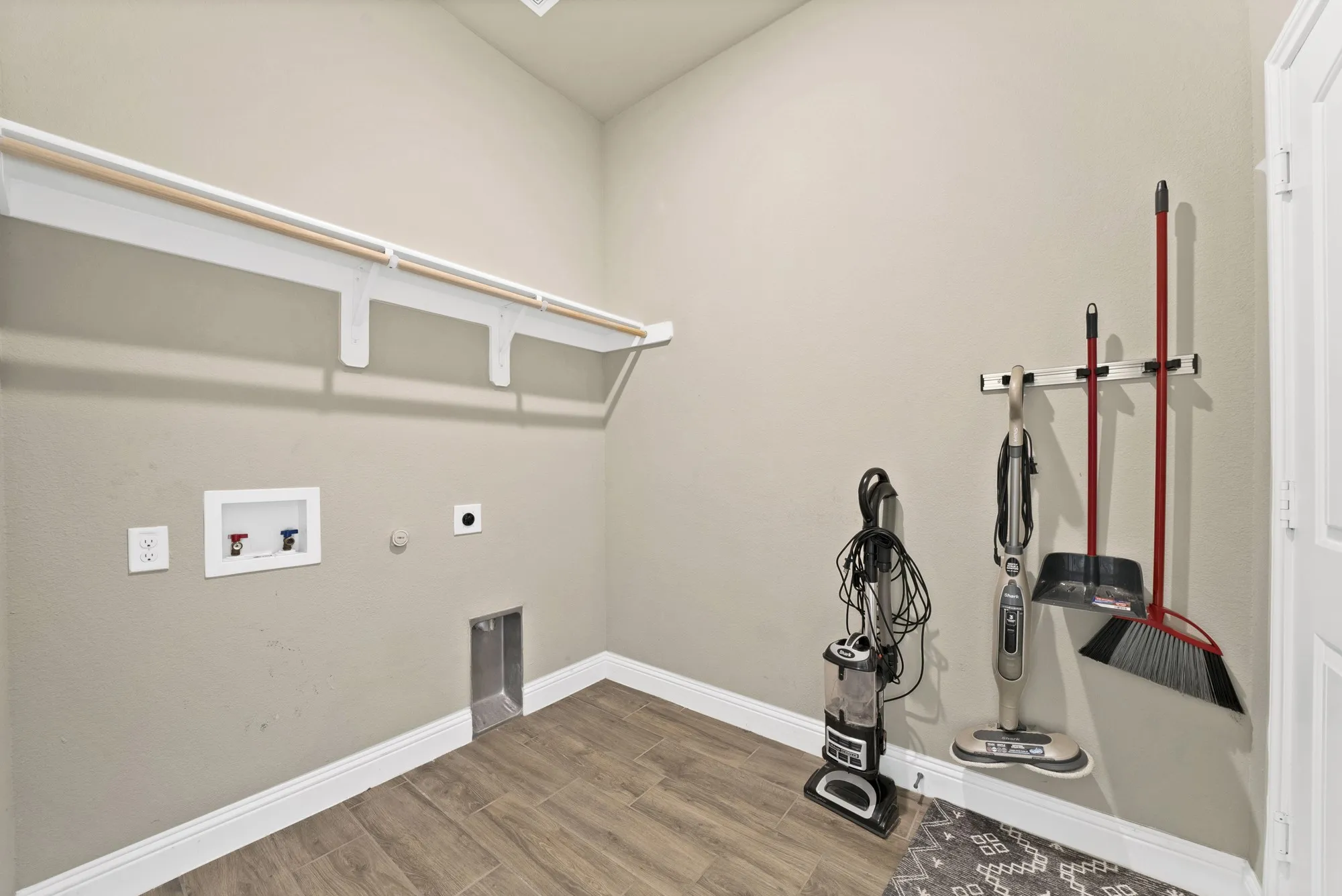 Utility room featuring wood-finish flooring, white baseboards, a built-in shelf with hanging rod, and appliance hookups
