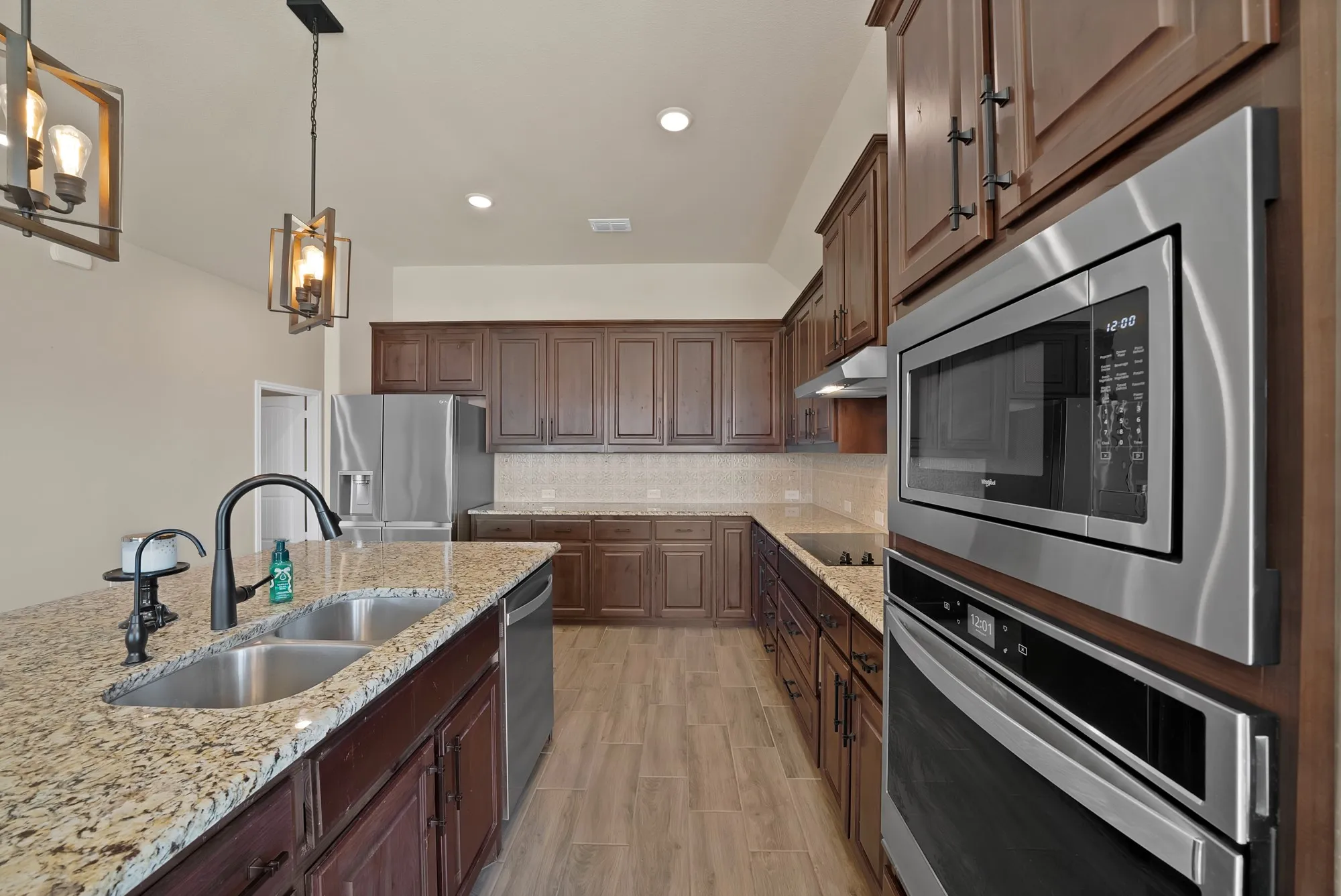 Kitchen featuring a large central island with a dual-basin stainless steel sink, granite countertops, and dark wood cabinetry