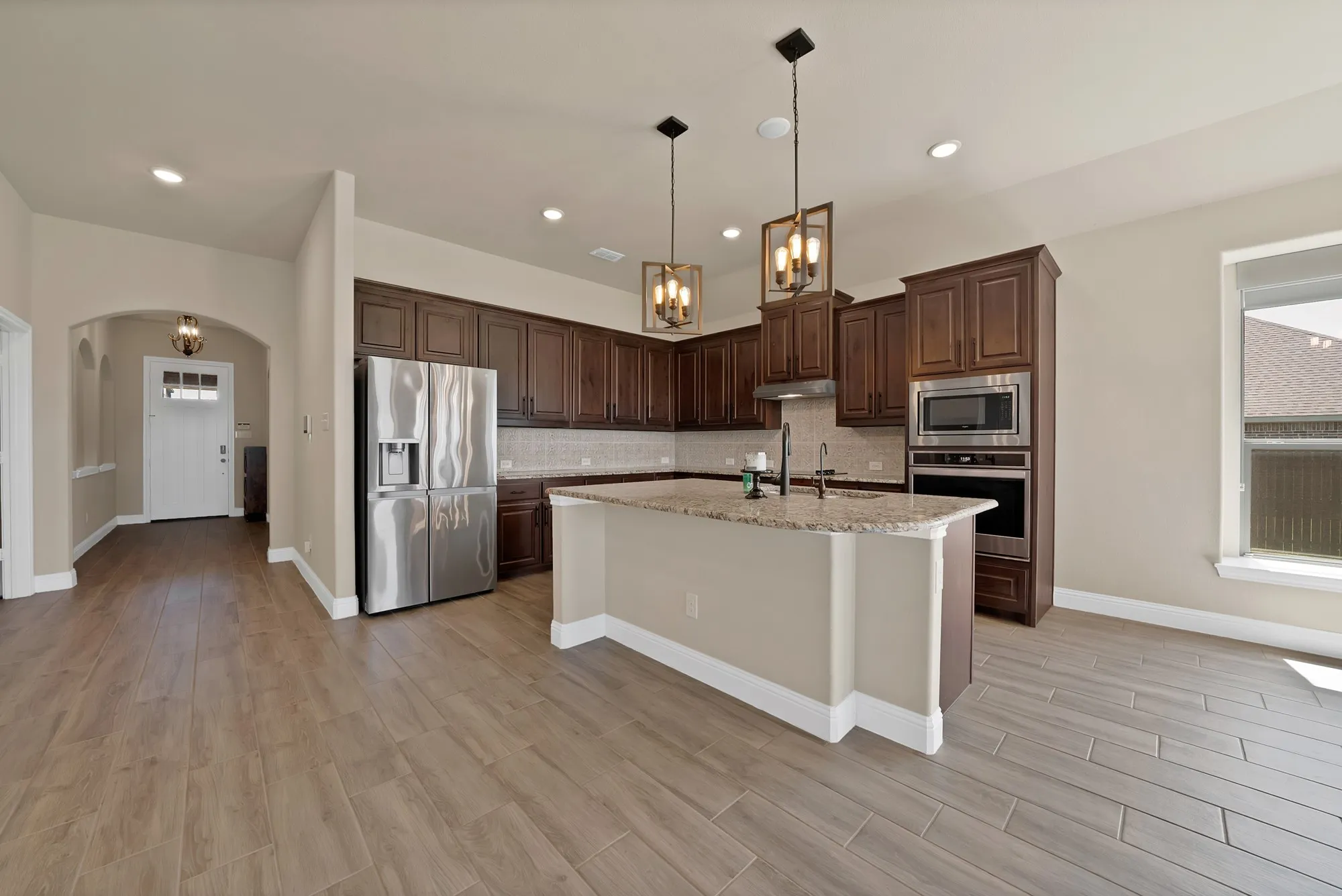 Open-concept kitchen featuring wood-finish tile flooring, a central island with granite countertop, dark wood cabinetry, and stainless steel appliances