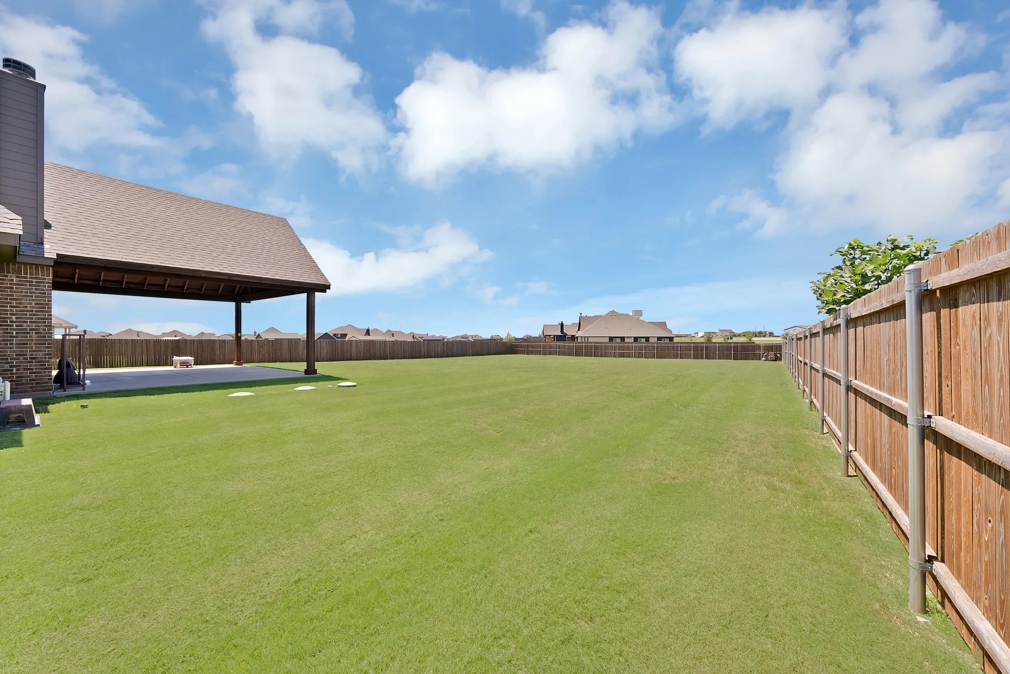 Spacious backyard featuring a manicured lawn, full wood privacy fence, and a covered patio with concrete flooring