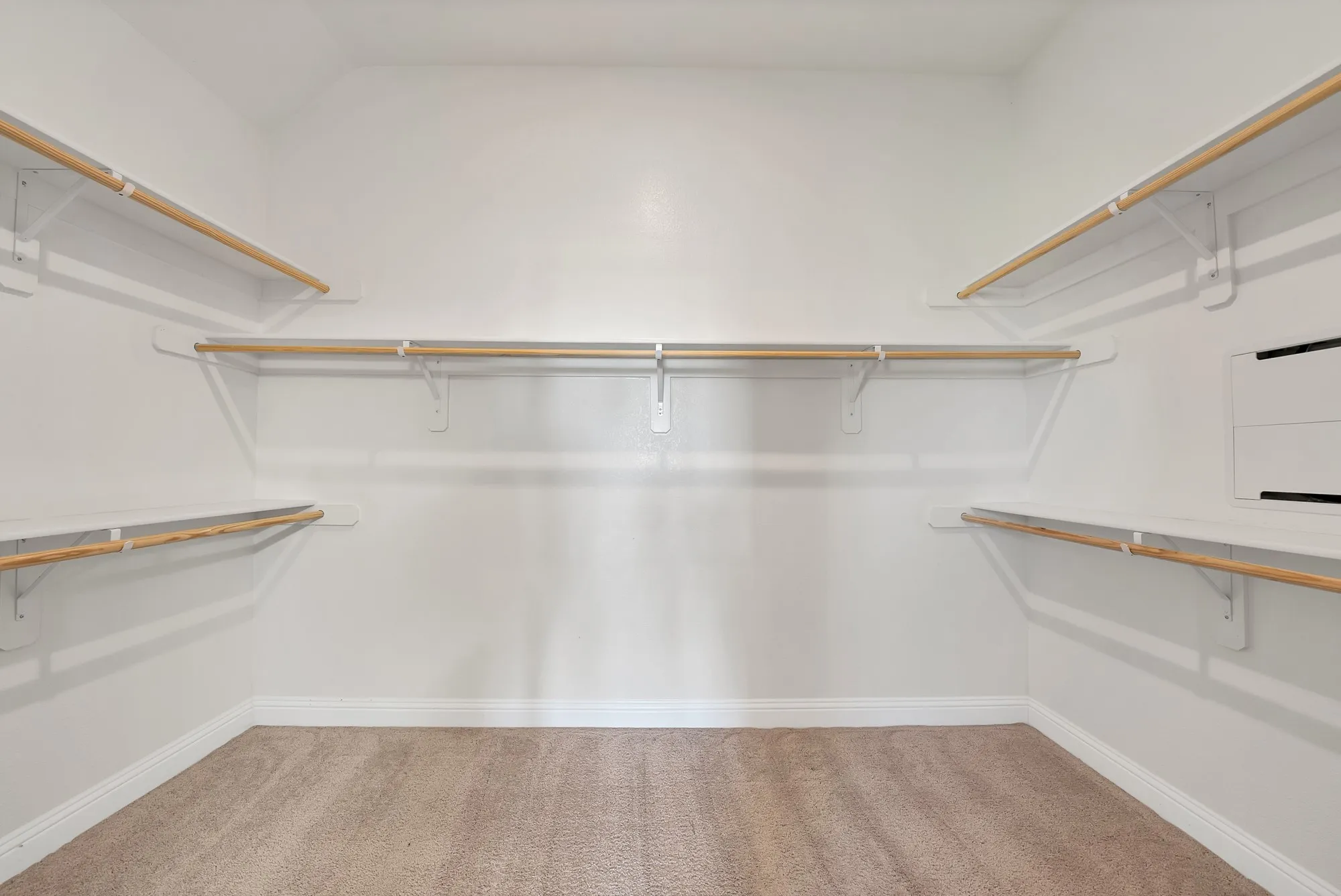 Walk-in closet featuring light beige carpet flooring, white baseboards, white walls, multiple built-in shelving units, and wooden clothing rods