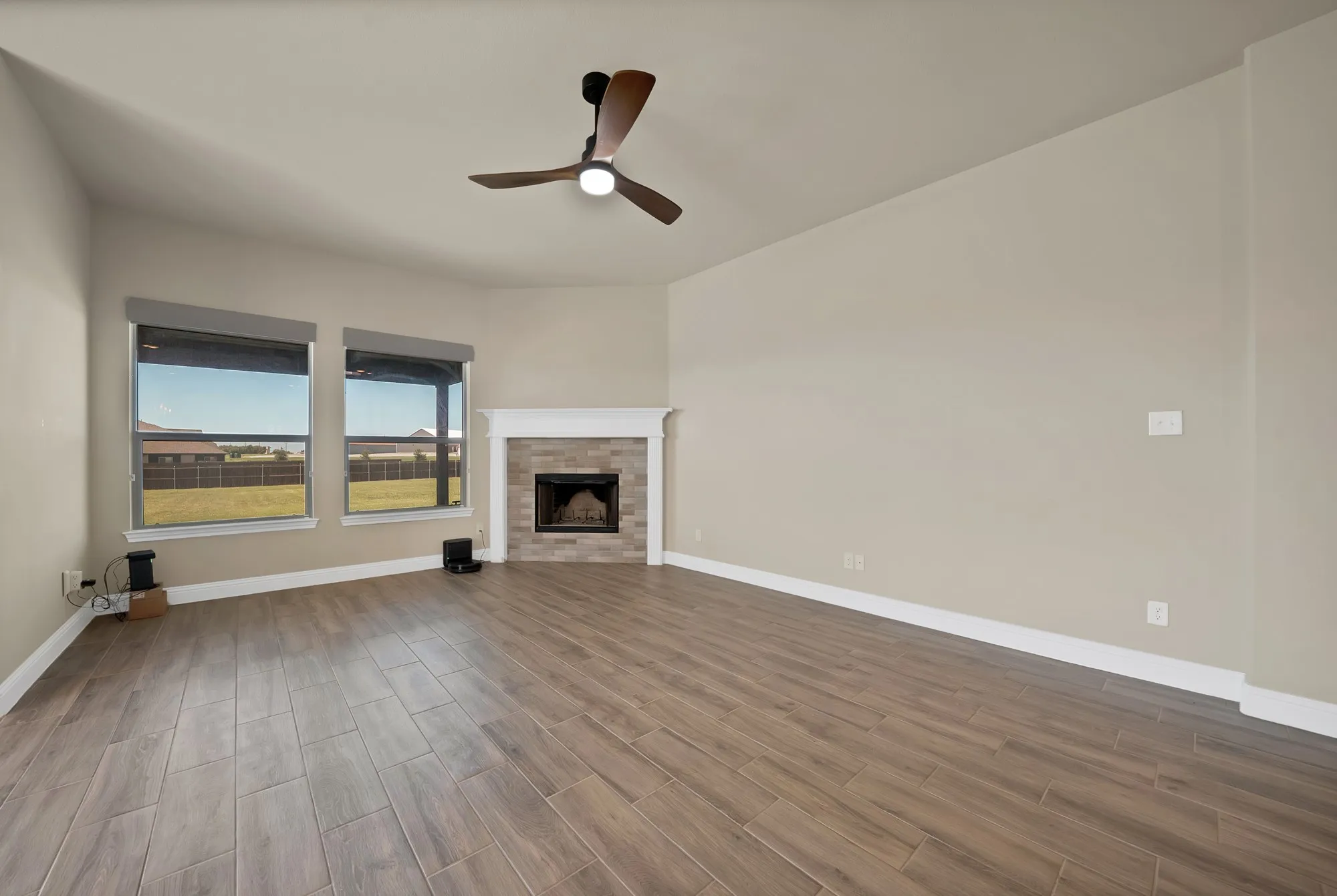 Spacious interior room featuring wood-finish flooring, a corner fireplace with stone surround and white mantel, and two large windows offering exterior views