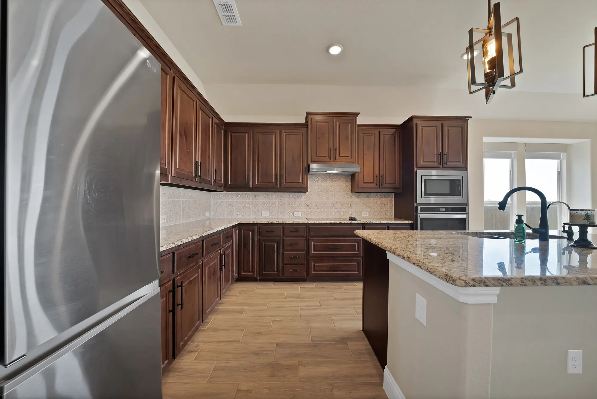 Gourmet kitchen featuring a large island, wood-finish flooring, stainless steel appliances, dark wood cabinetry, and light-toned countertops