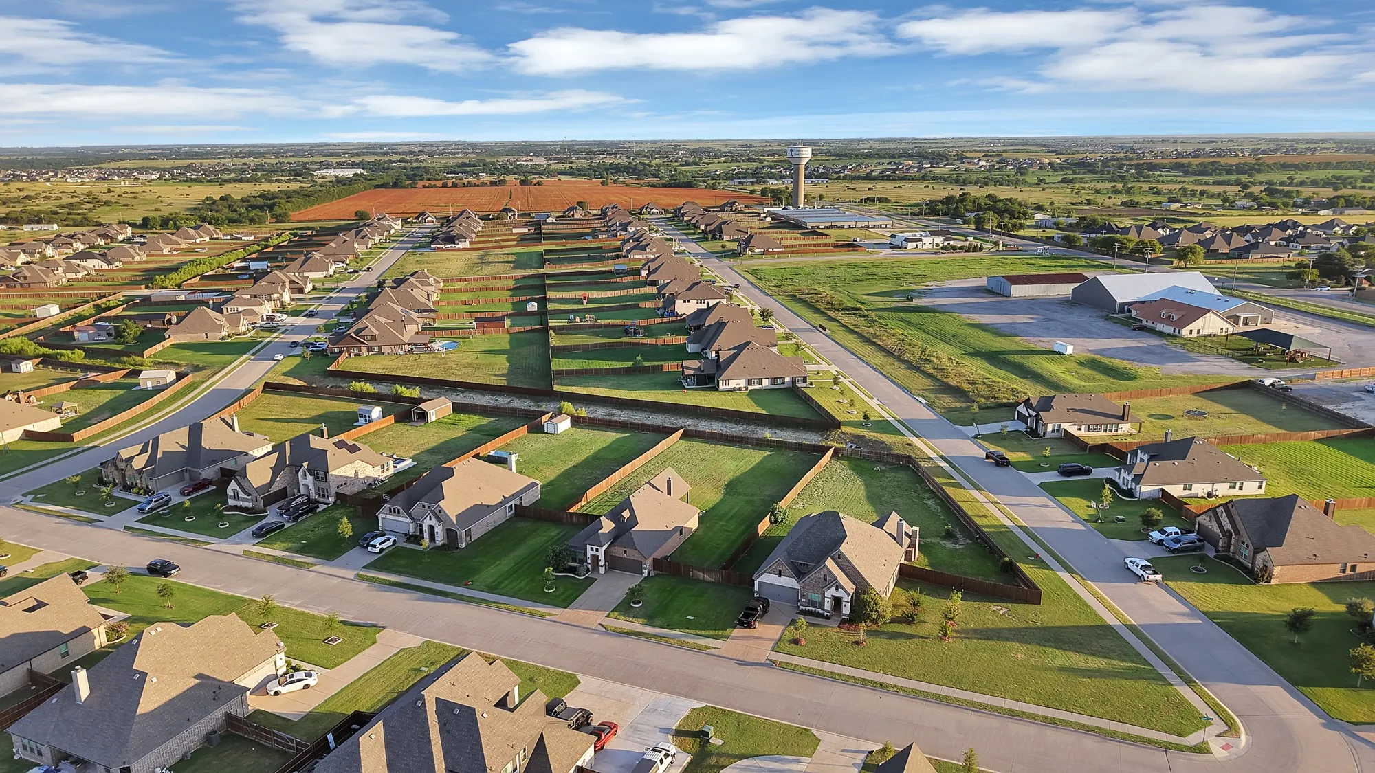 Aerial perspective showcasing a residential development with numerous single-story homes, expansive green lawns, and paved streets