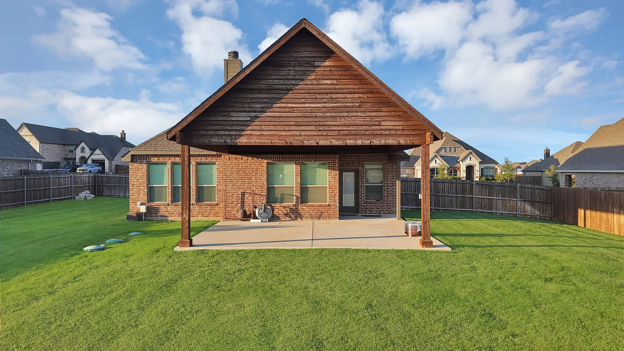 Expansive backyard featuring a covered patio with a wood-finish ceiling, brick exterior, multiple windows, and a privacy fence