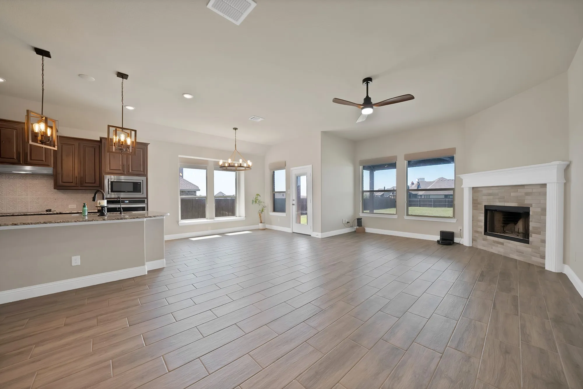 Expansive open-concept living space with wood-finish flooring, a corner fireplace featuring a tile surround and mantel, and a ceiling fan