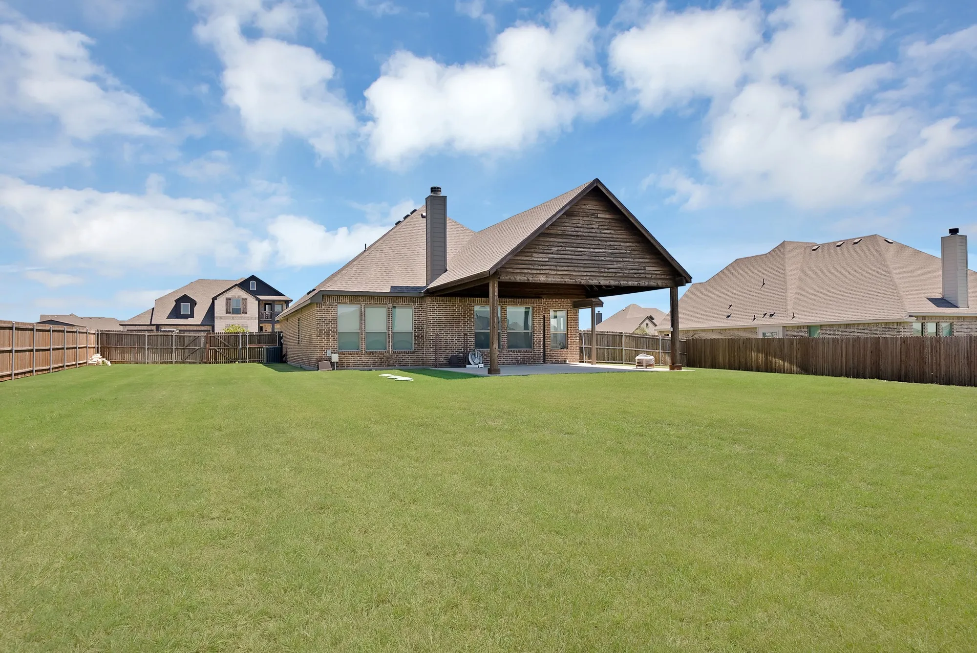 Expansive rear lawn featuring a covered patio with a vaulted wood-paneled ceiling, a brick exterior, and a privacy fence