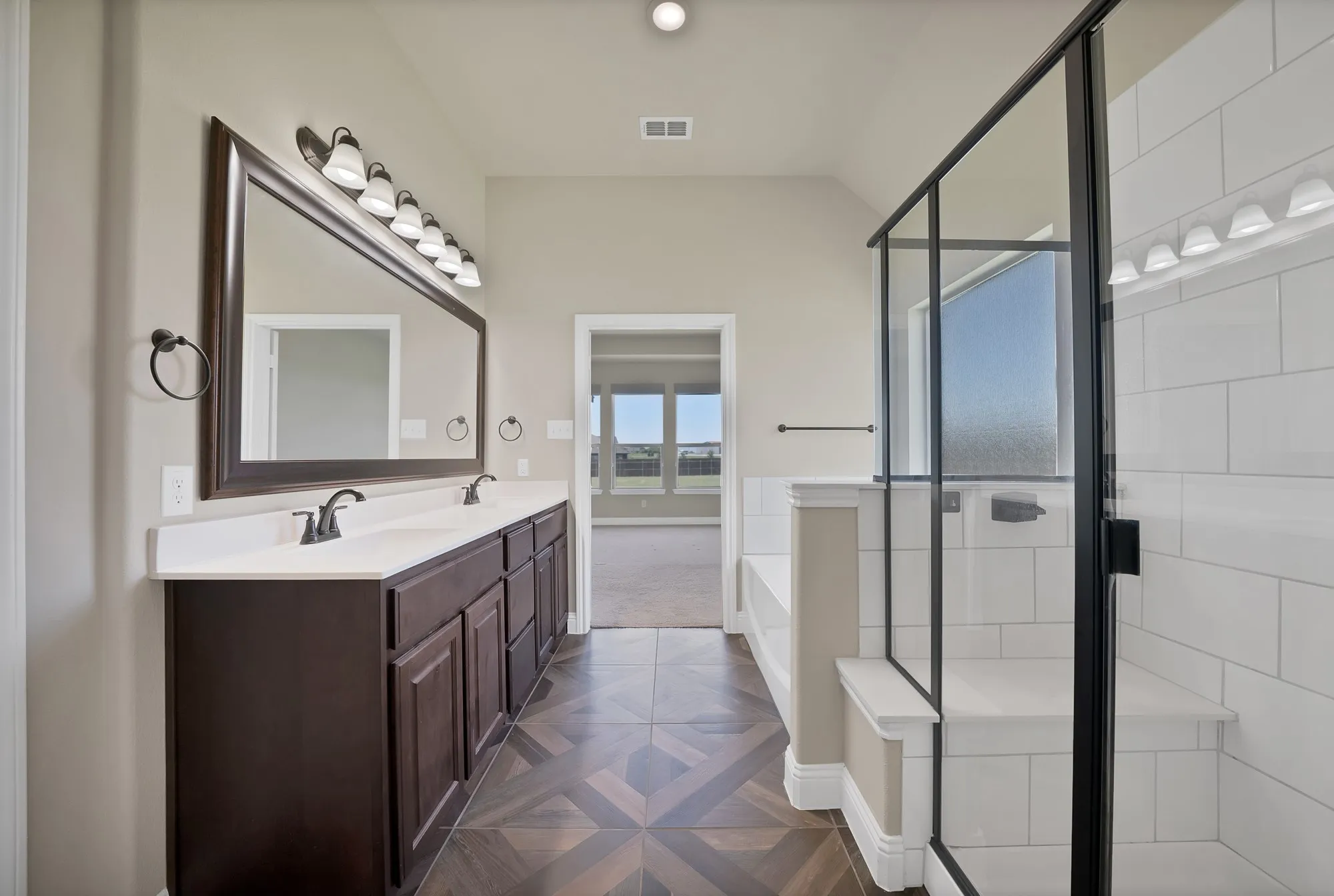 Spacious bathroom featuring a double vanity with dark wood cabinetry and dual sinks, a large framed mirror, and a walk-in shower with black-framed glass and white subway tile surround