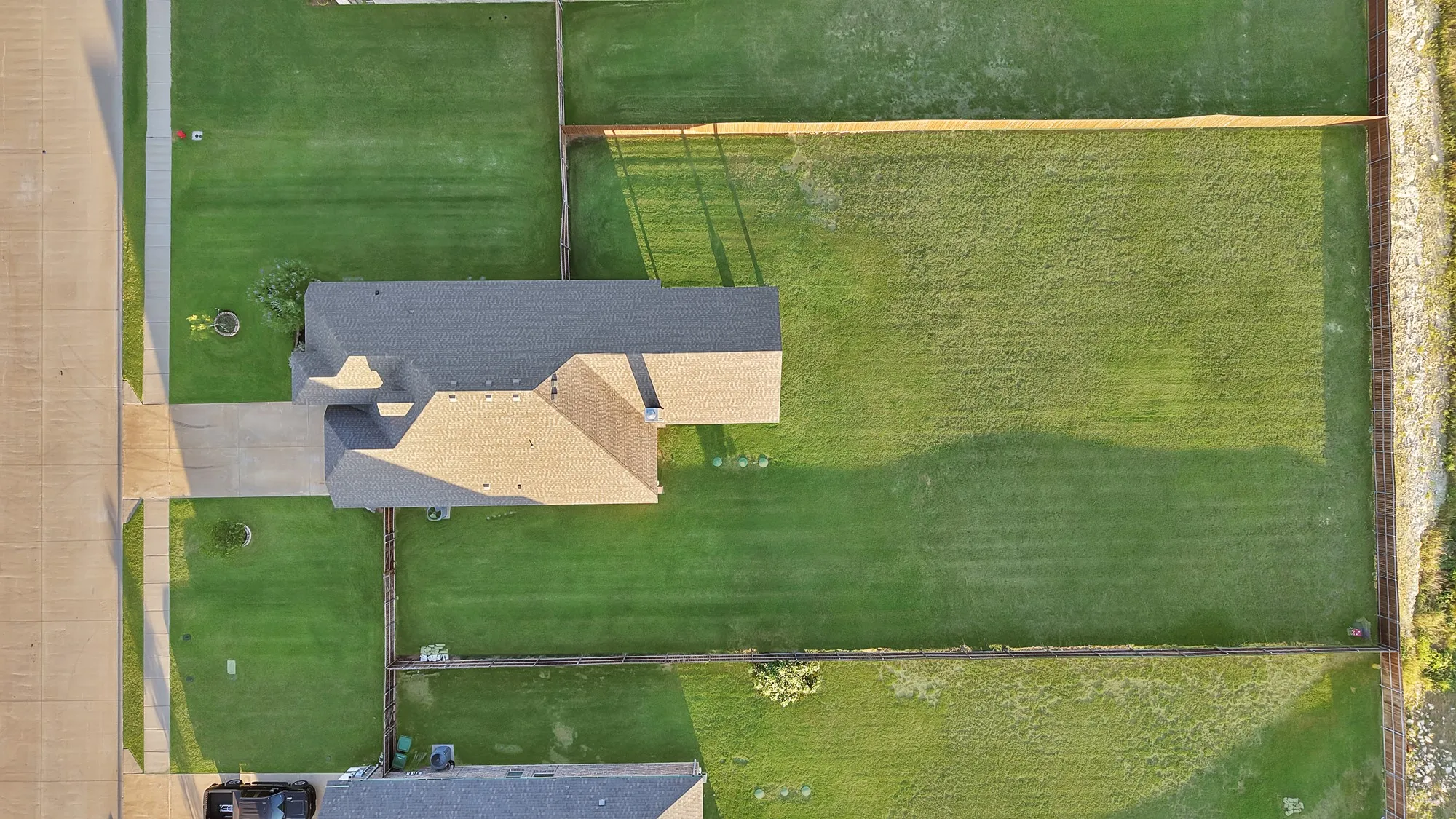 Expansive property featuring a gabled roofline, concrete driveway, and a substantial fenced backyard with mature trees