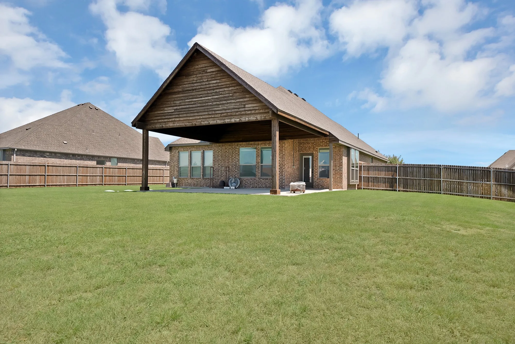 Spacious lawn with a covered patio featuring a wood-plank ceiling and brick exterior