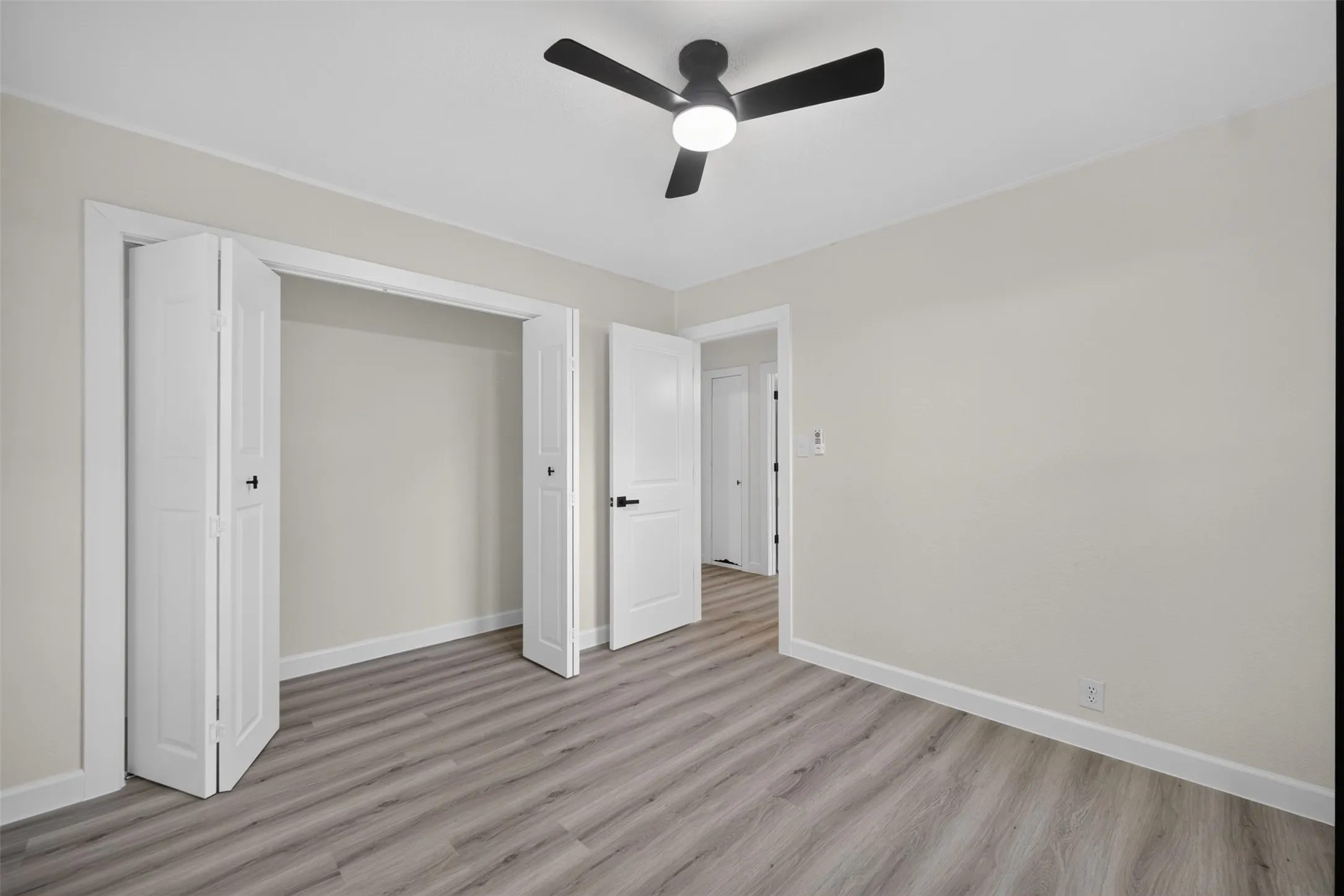 Bedroom featuring light-toned walls, wood-finish flooring, a contemporary ceiling fan with integrated lighting, and a closet with bi-fold doors