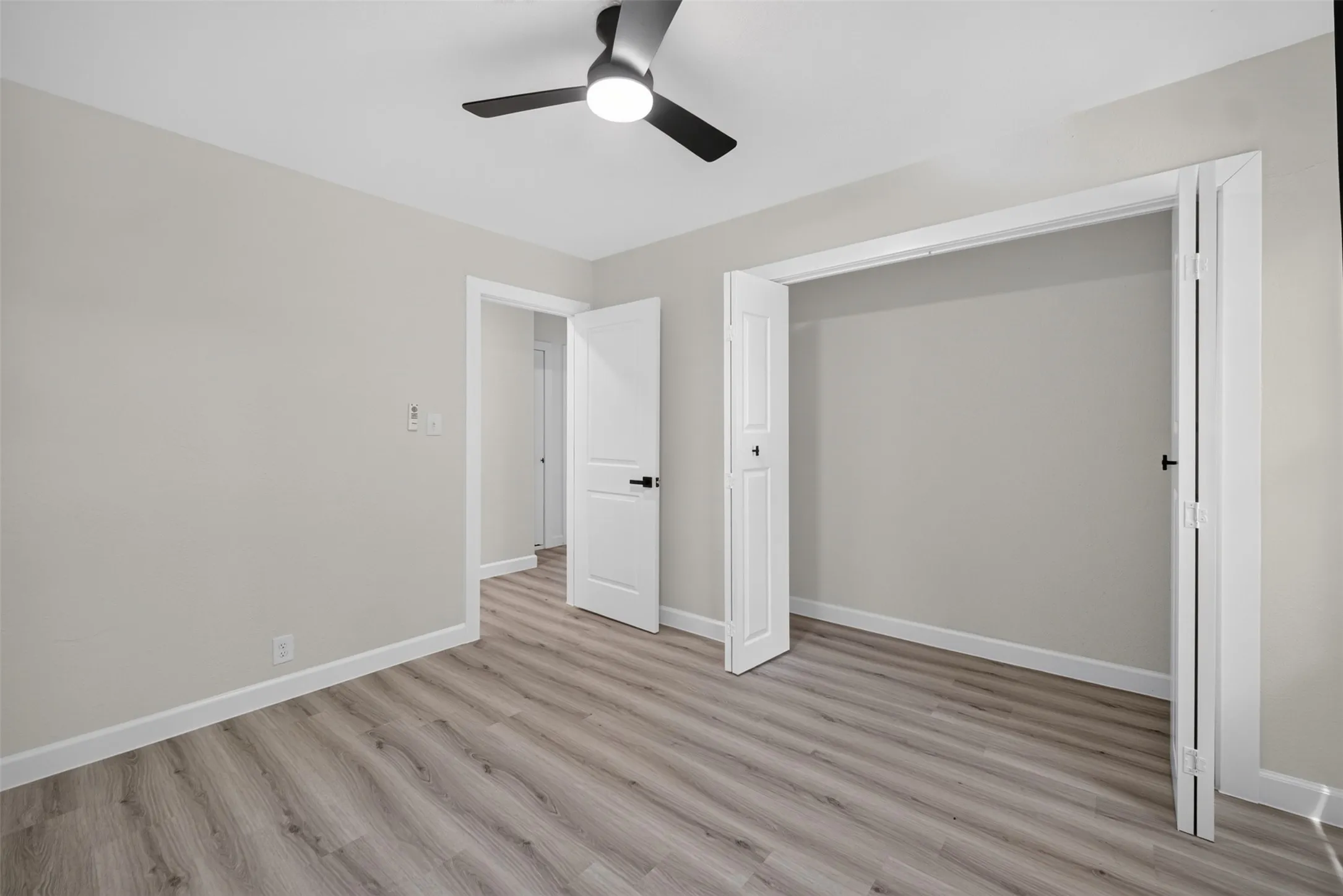 Spacious room featuring wood-finish flooring, light gray wall paint, and white baseboards