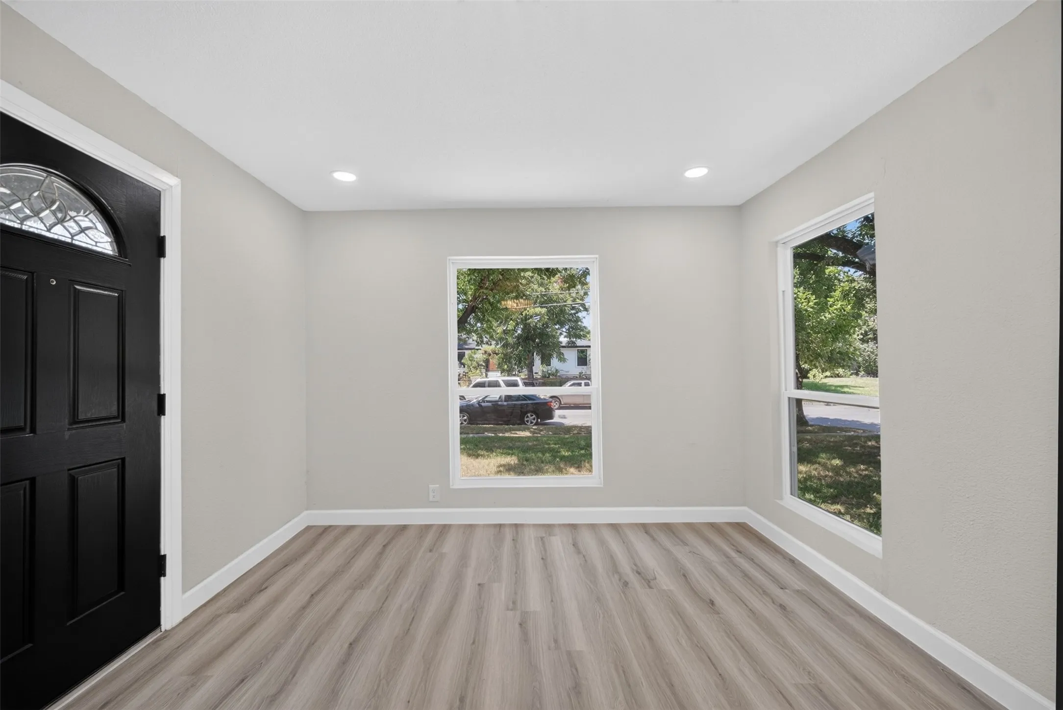 Entryway featuring a decorative transom window above a paneled door, wood-finish flooring, two large windows, recessed ceiling lighting, and white baseboards