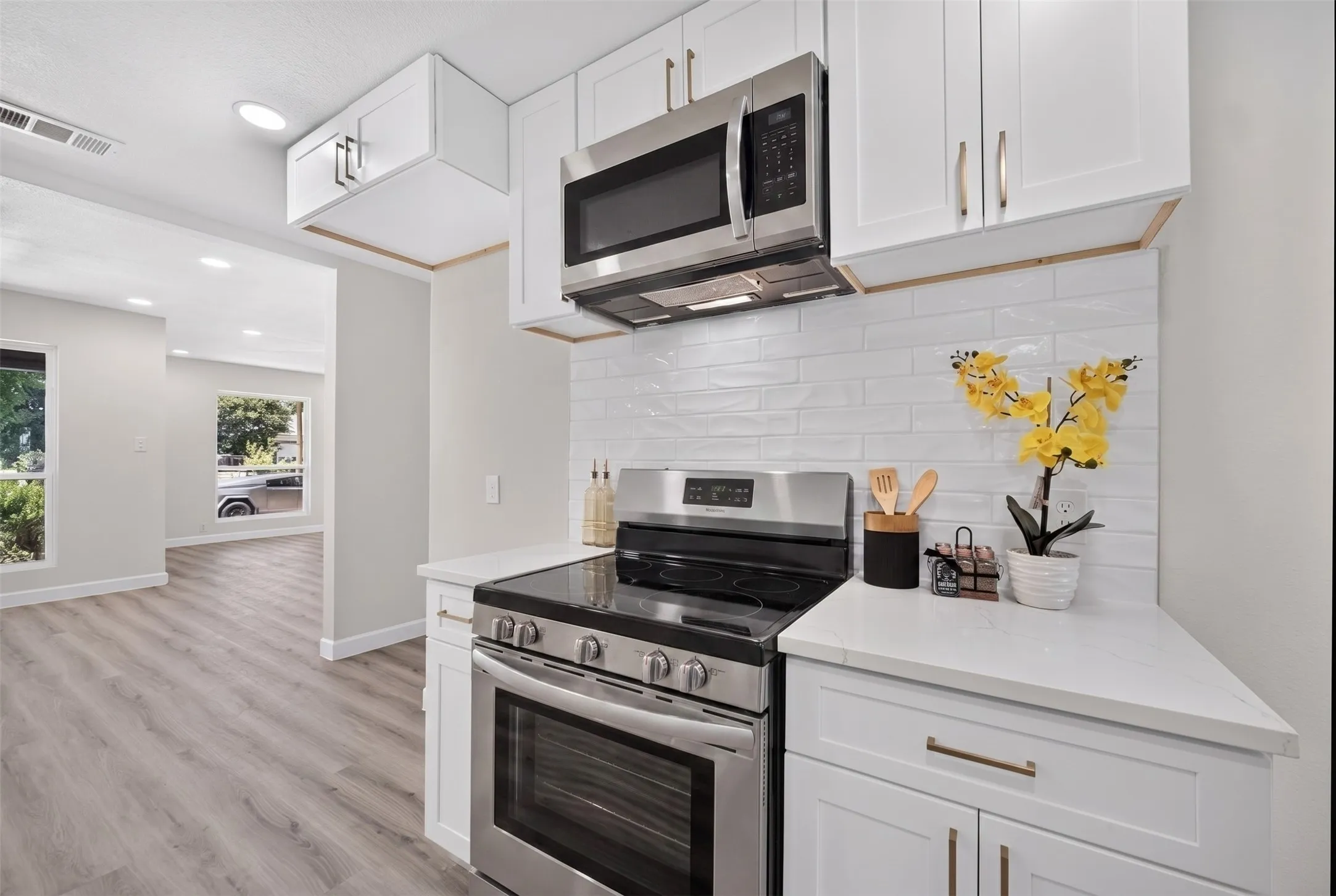 Modern kitchen featuring white shaker cabinetry with brushed gold hardware, stainless steel appliances, and quartz countertops