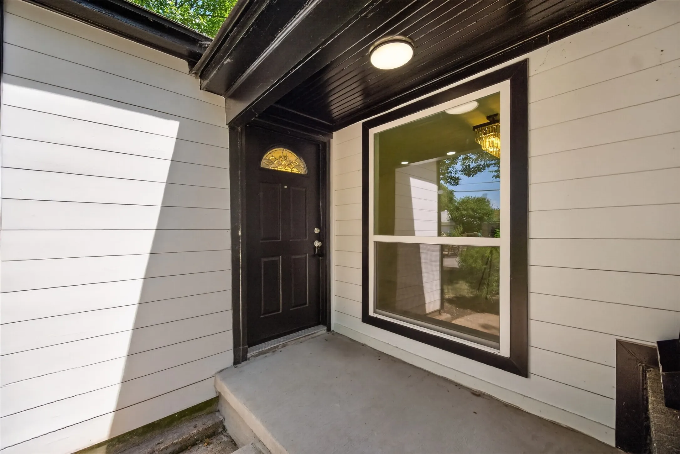 Entryway featuring white horizontal siding, a dark paneled door with an arched decorative glass insert, and a prominent window with dark trim