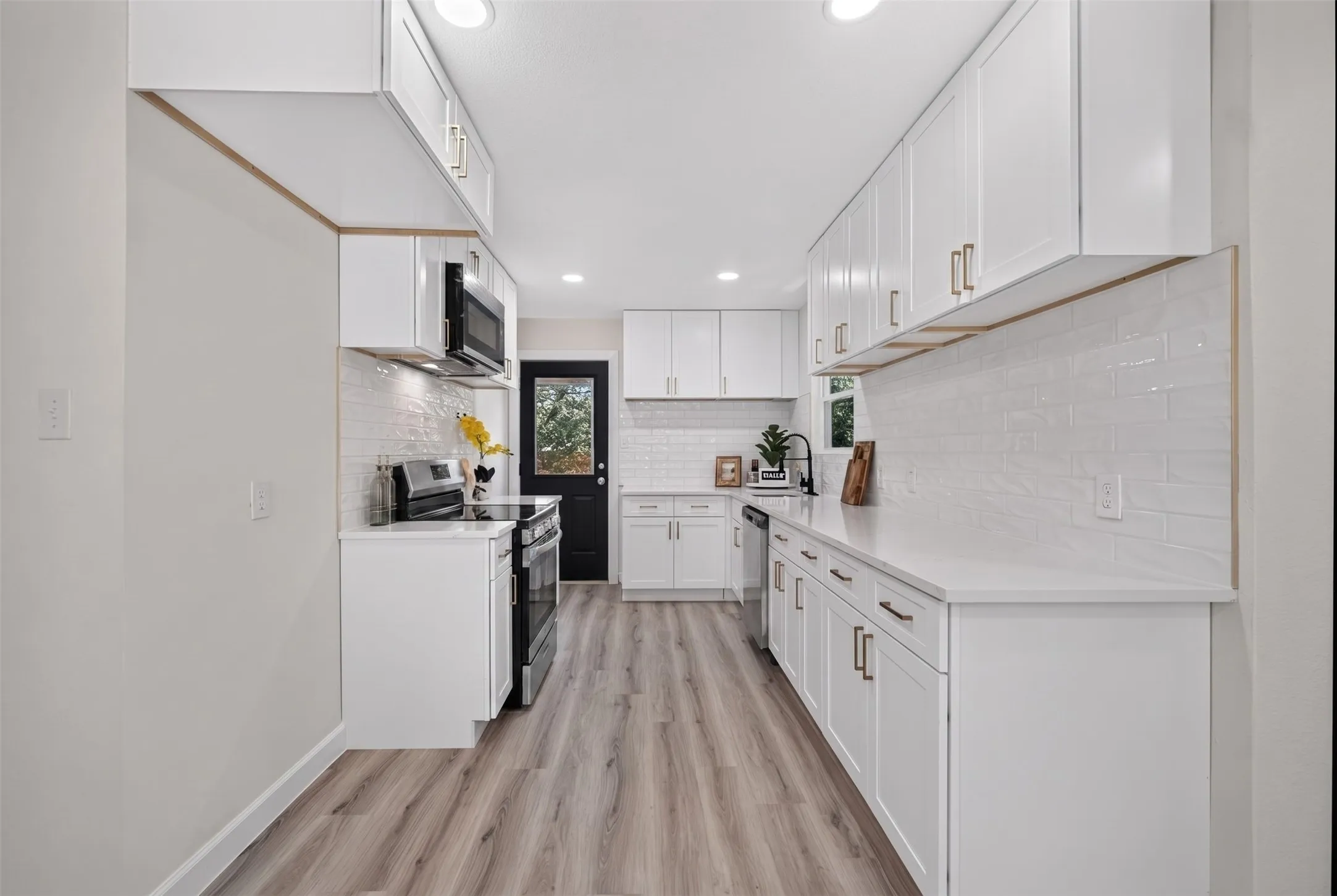 Galley kitchen featuring white cabinetry with gold-toned hardware, solid surface countertops, and an integrated microwave