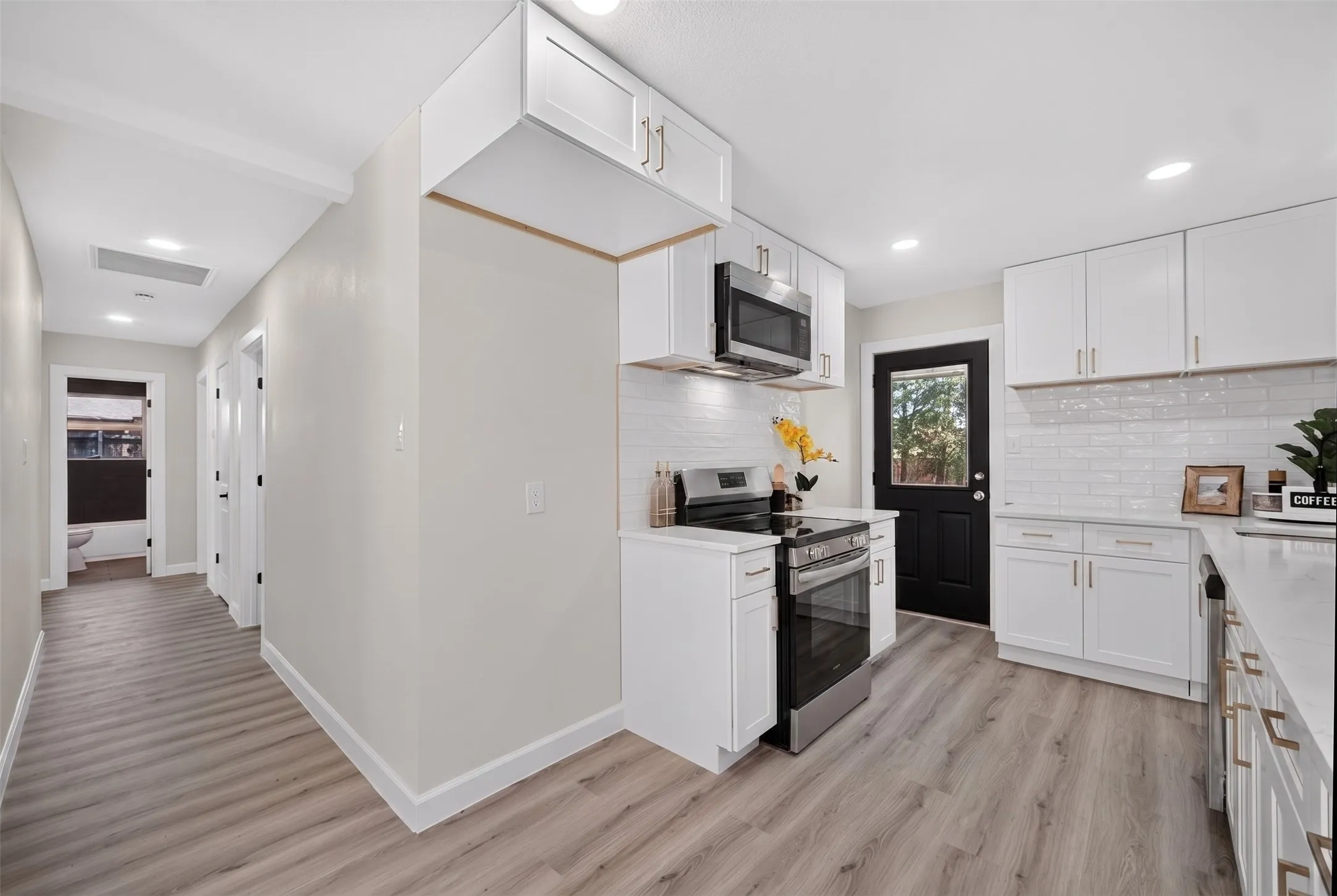 Modern kitchen featuring white shaker cabinetry with gold-tone hardware, stainless steel appliances, a white subway tile backsplash, and light wood-finish flooring