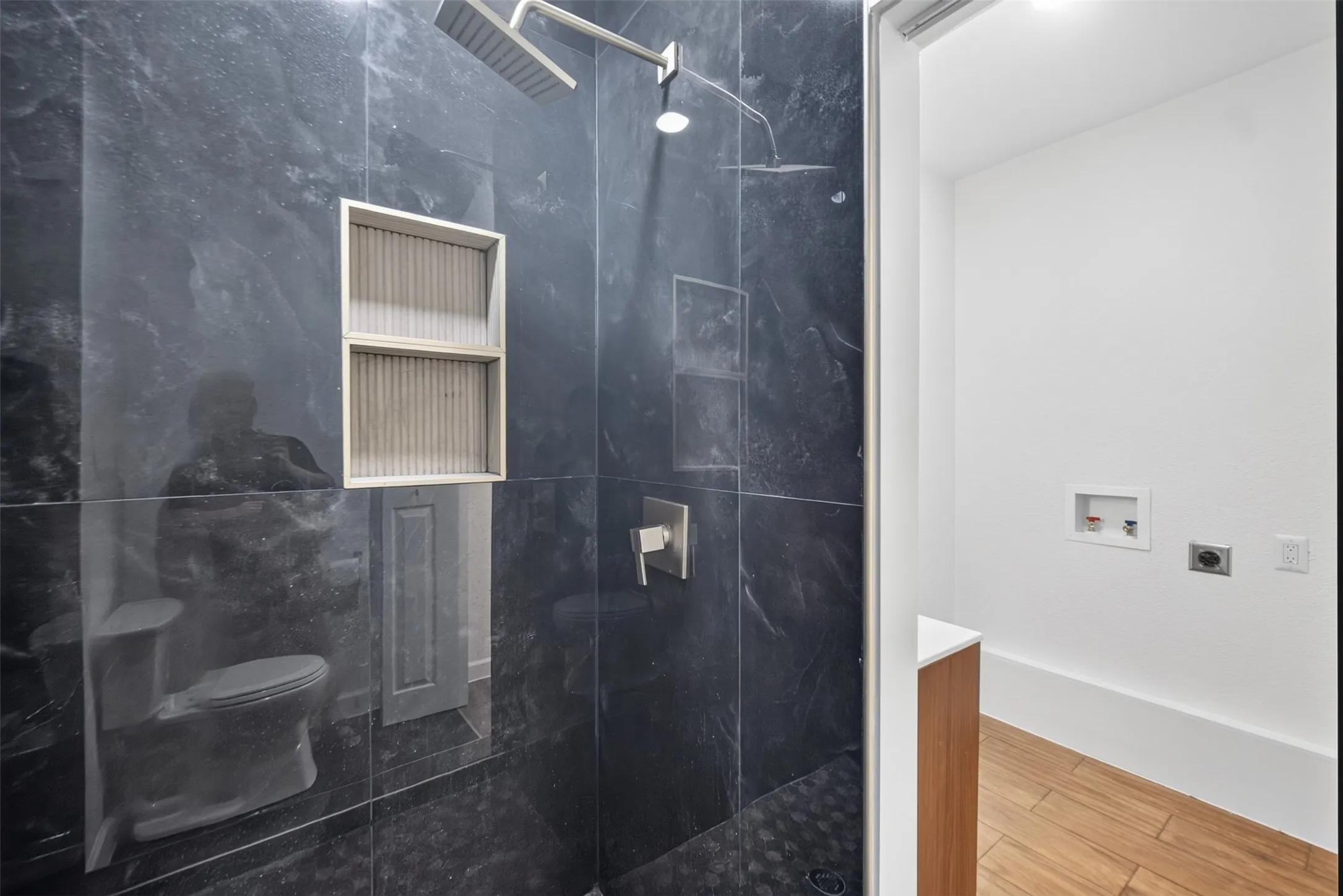 Walk-in shower featuring dark-toned tiled walls, dual showerheads, and recessed shelving