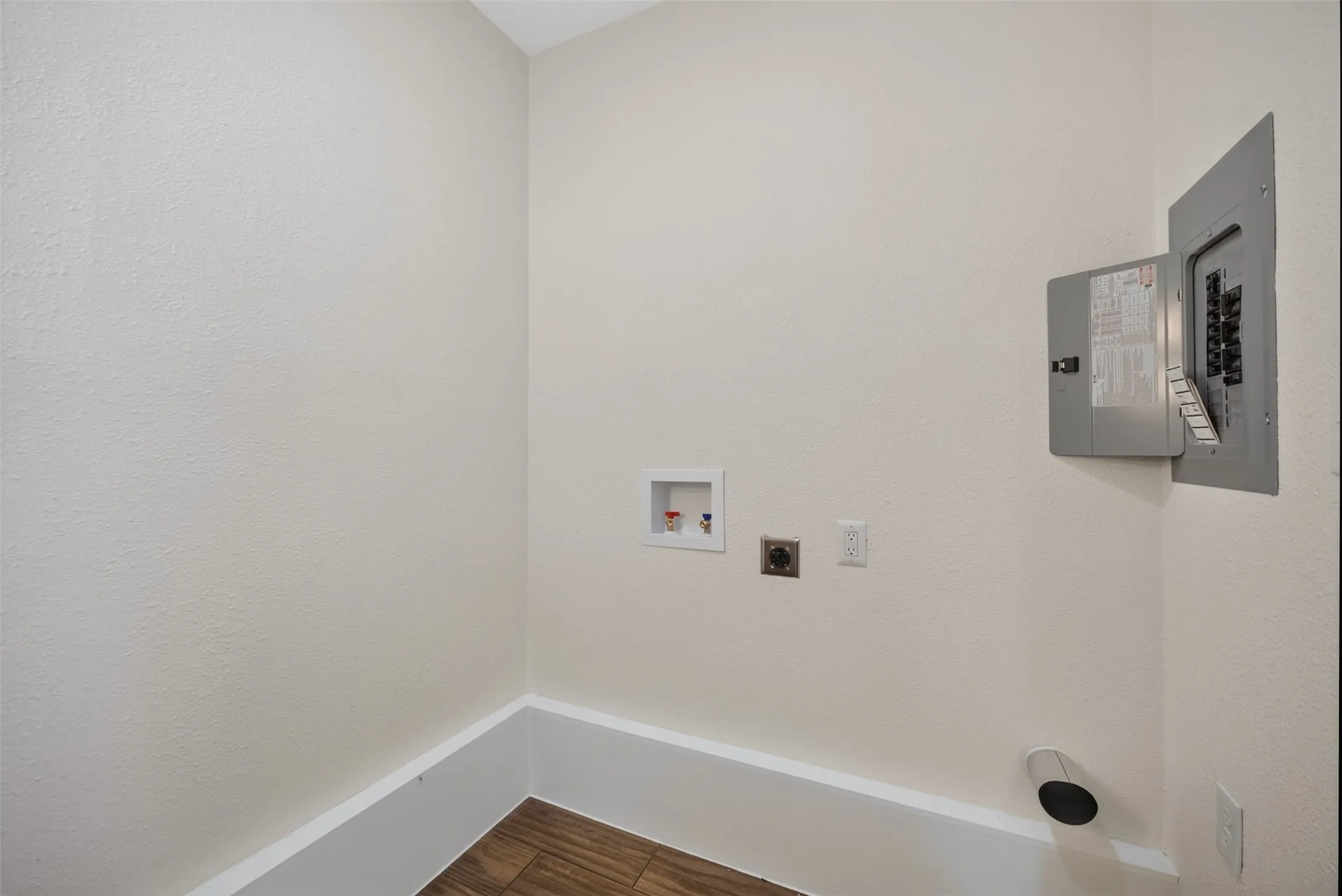 Laundry area with wood-finish flooring, white baseboards, and neutral-toned walls