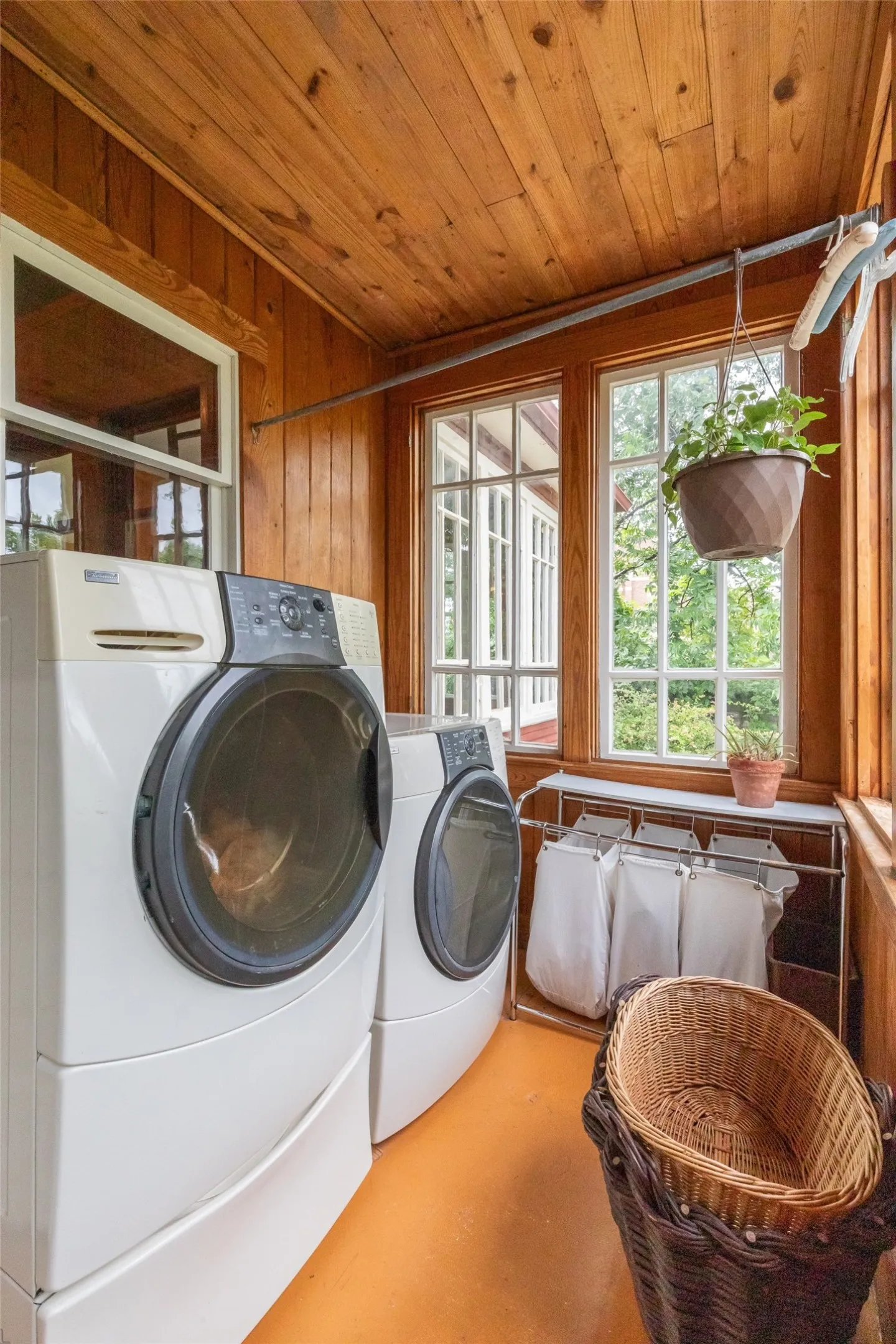 Dedicated laundry area featuring wood-paneled walls and ceiling, multiple windows, and a durable orange-hued floor