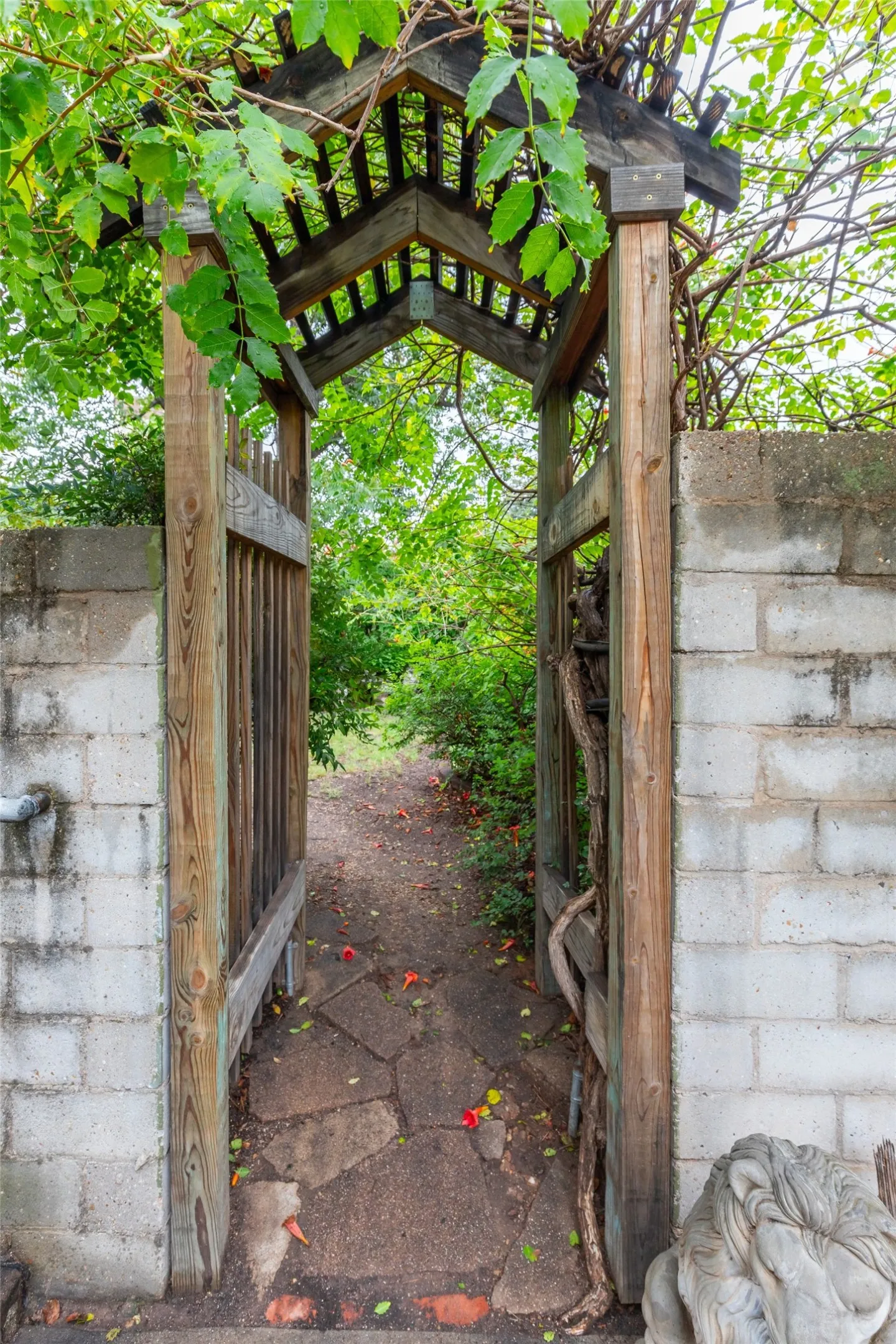 Gated entry featuring a wooden arbor with natural vine coverage, flanked by a concrete block wall to secret garden