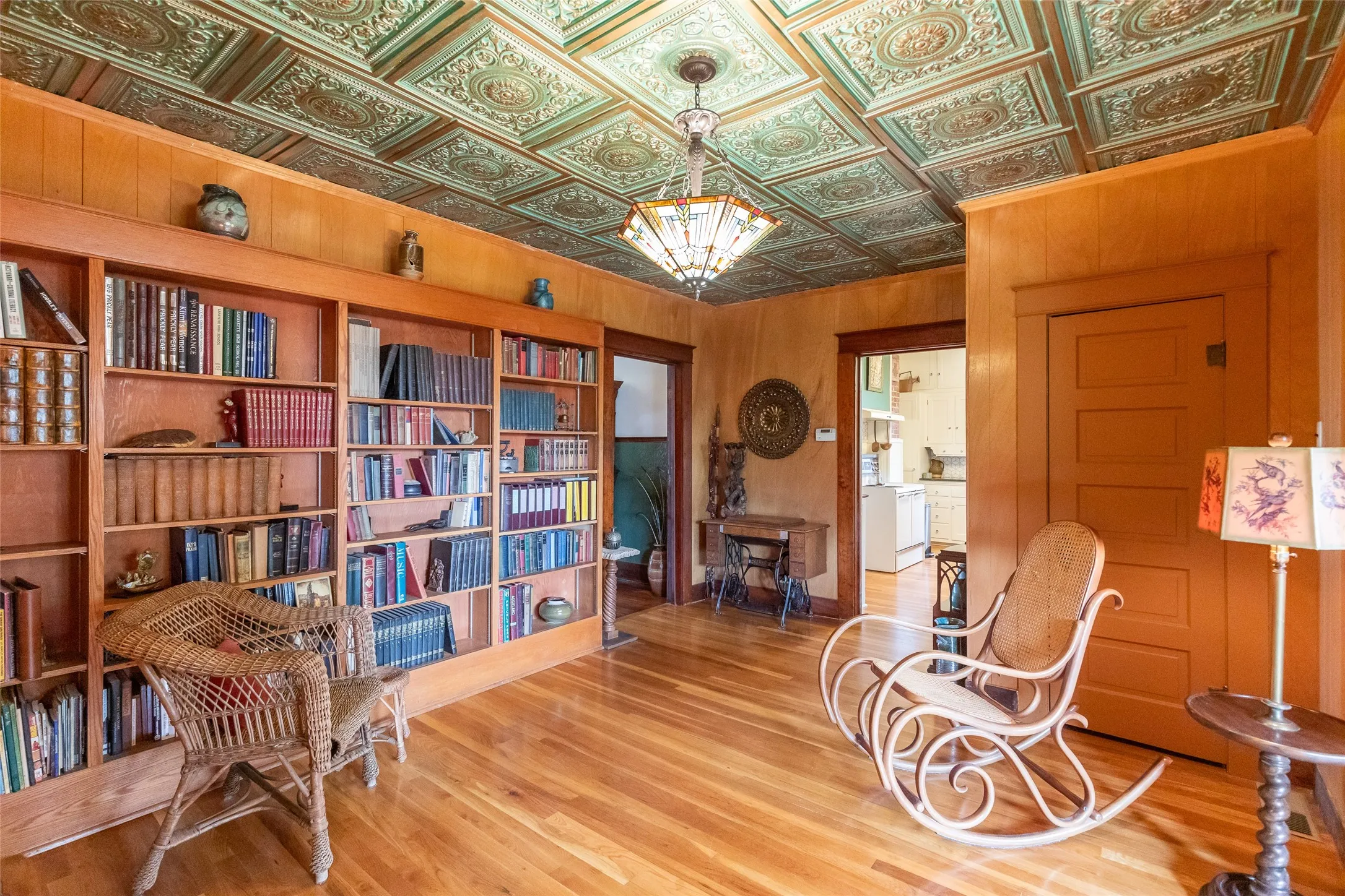 Ornate pressed tin ceiling with a decorative chandelier, built-in wooden bookshelves, warm wood-finish flooring, and paneled walls