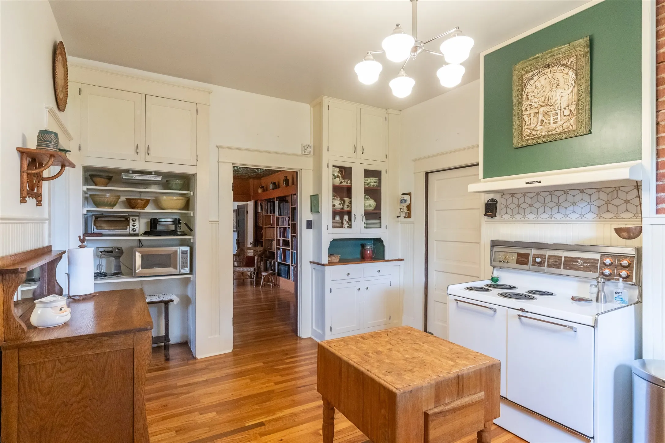 Kitchen featuring hardwood flooring, white cabinetry, a built-in oven range with a patterned backsplash, a central butcher block island, and recessed shelving