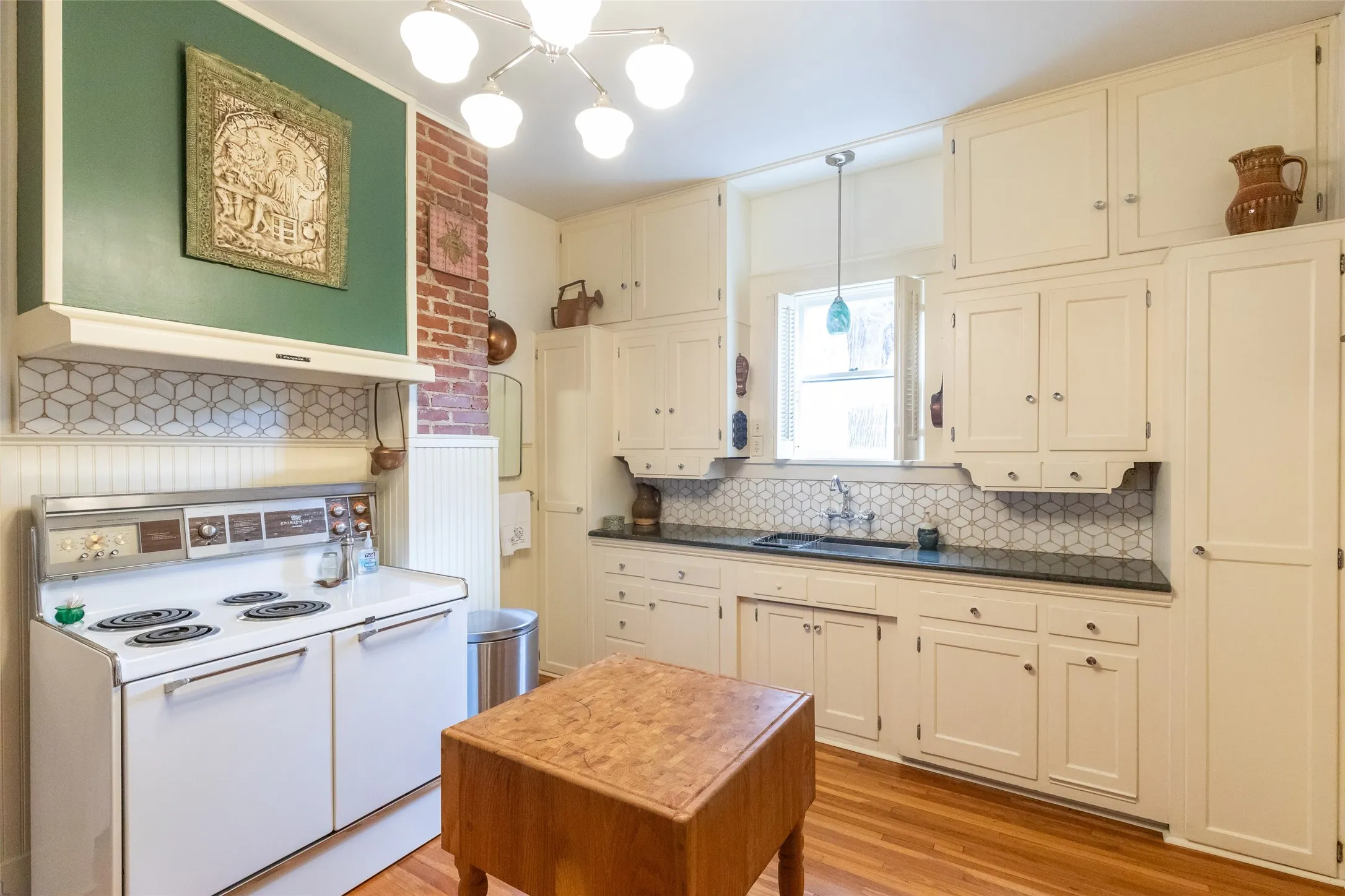 Kitchen featuring white cabinetry, wood-finish flooring, black countertops, and a white hexagonal tile backsplash