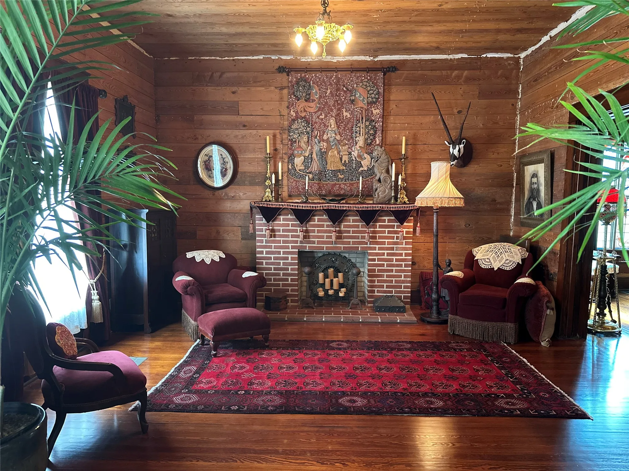 Living area featuring wood paneling, wood-finish flooring, a brick fireplace with a detailed mantel, and a multi-light ceiling fixture