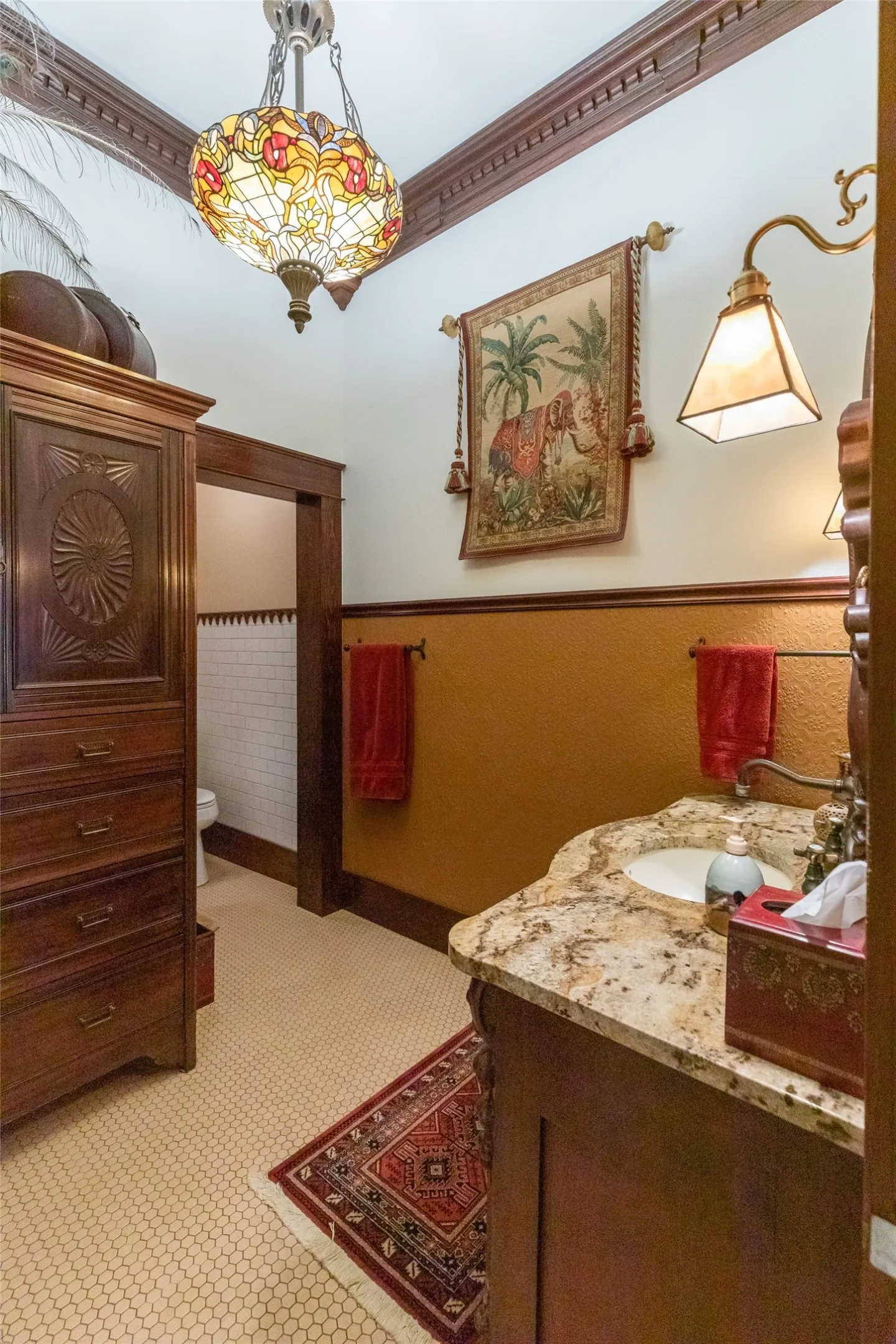 Bathroom featuring a decorative stained-glass ceiling fixture, ornate wood trim, a single vanity with a stone countertop, and light-colored hexagonal floor tiling
