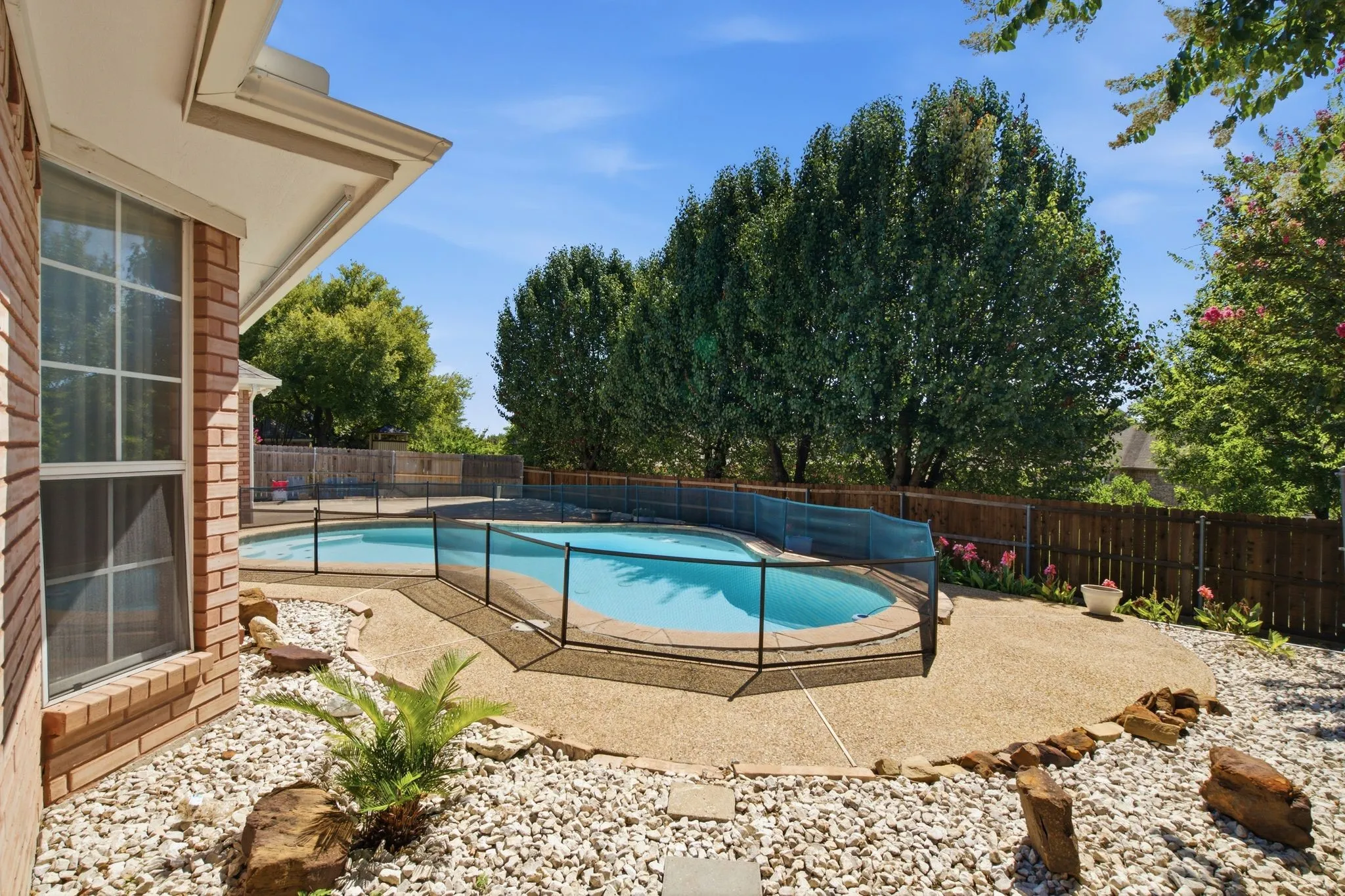 Backyard oasis featuring a fenced swimming pool with a safety barrier, exposed aggregate patio, and natural stone landscaping